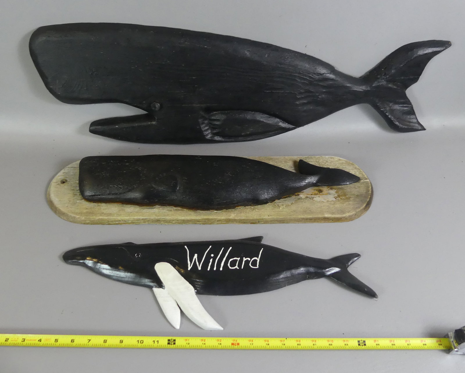 3 VINTAGE WOOD WHALE PLAQUES: Lot of 3 black carved wood whale plaques to 34 in long: Largest has presentation on back from 1966; 27 in on oval plaque; and smaller identified WILLARD and signed Randy Fisher, Dennis MA on back.