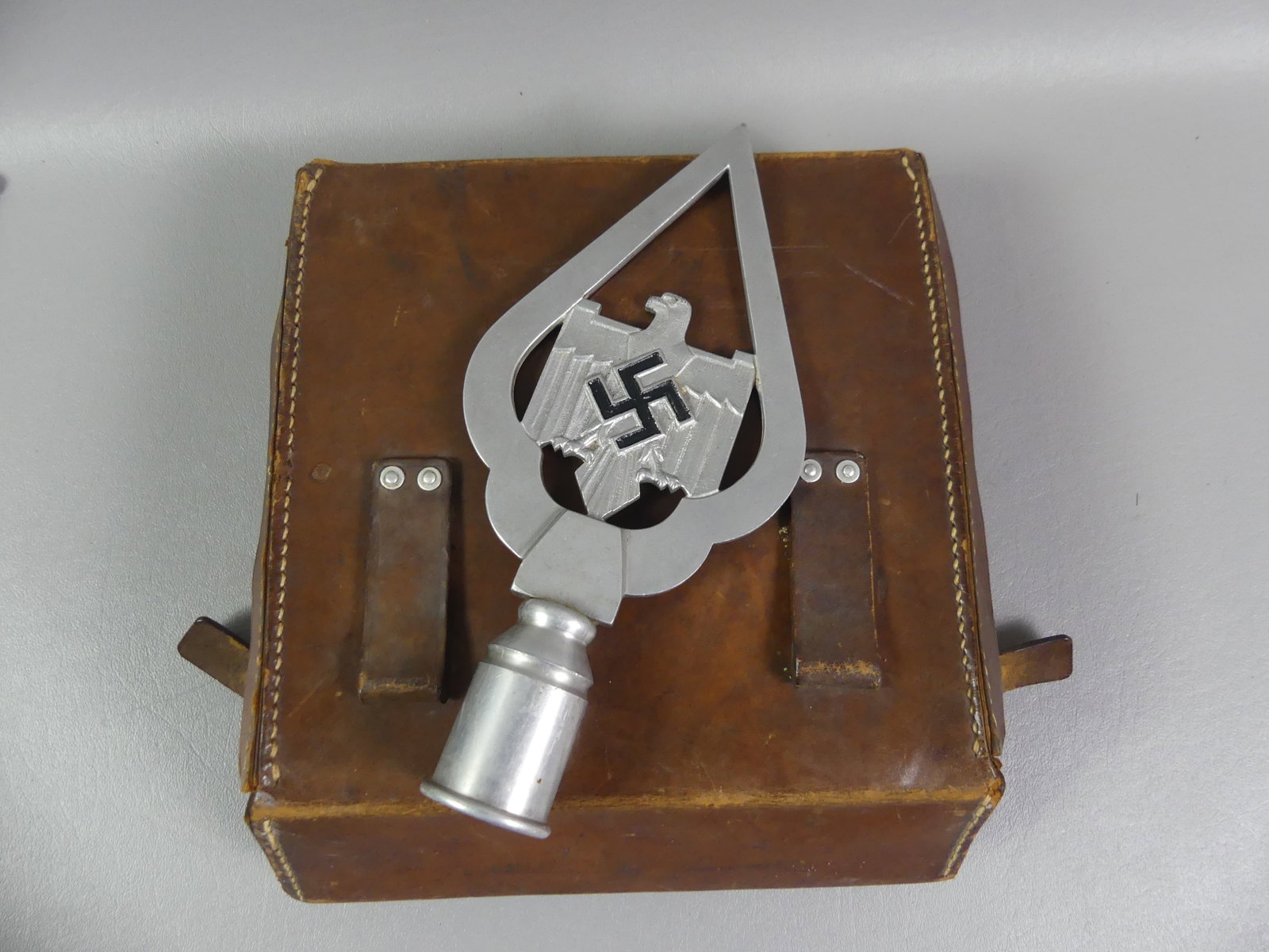 GERMAN WWII FLAG TOPPER & MEDICAL BOX: Scarce German WWII aluminum flag pole topper with eagle and swastika (9 in tall) together with an empty leather medical / drug kit, 8 in square.