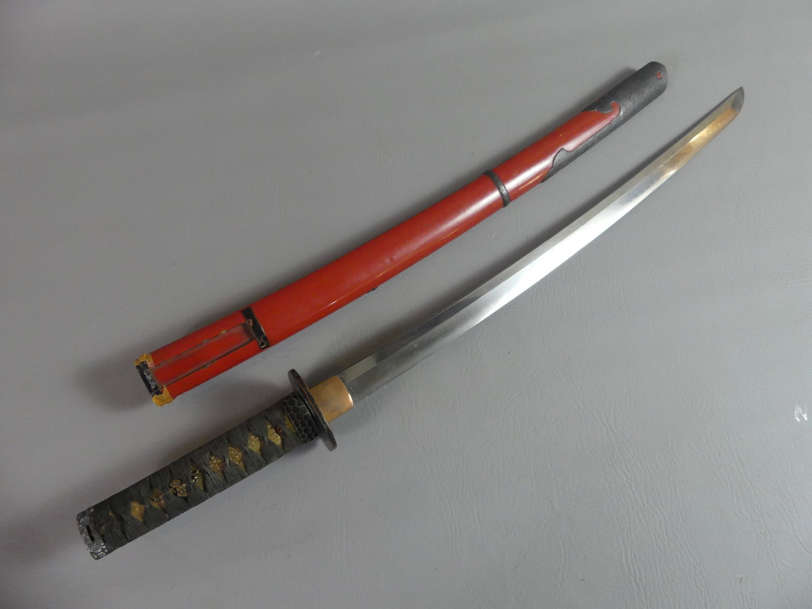JAPANESE WAKIZASHI SWORD: A Japanese Wakizashi sword sword taken from a soldier in WWII. It has a 22 in long sharp blade, overall 29 in. Bronze tsuba and black cord-wrapped sharkskin handle with decorative floral mounts. The r