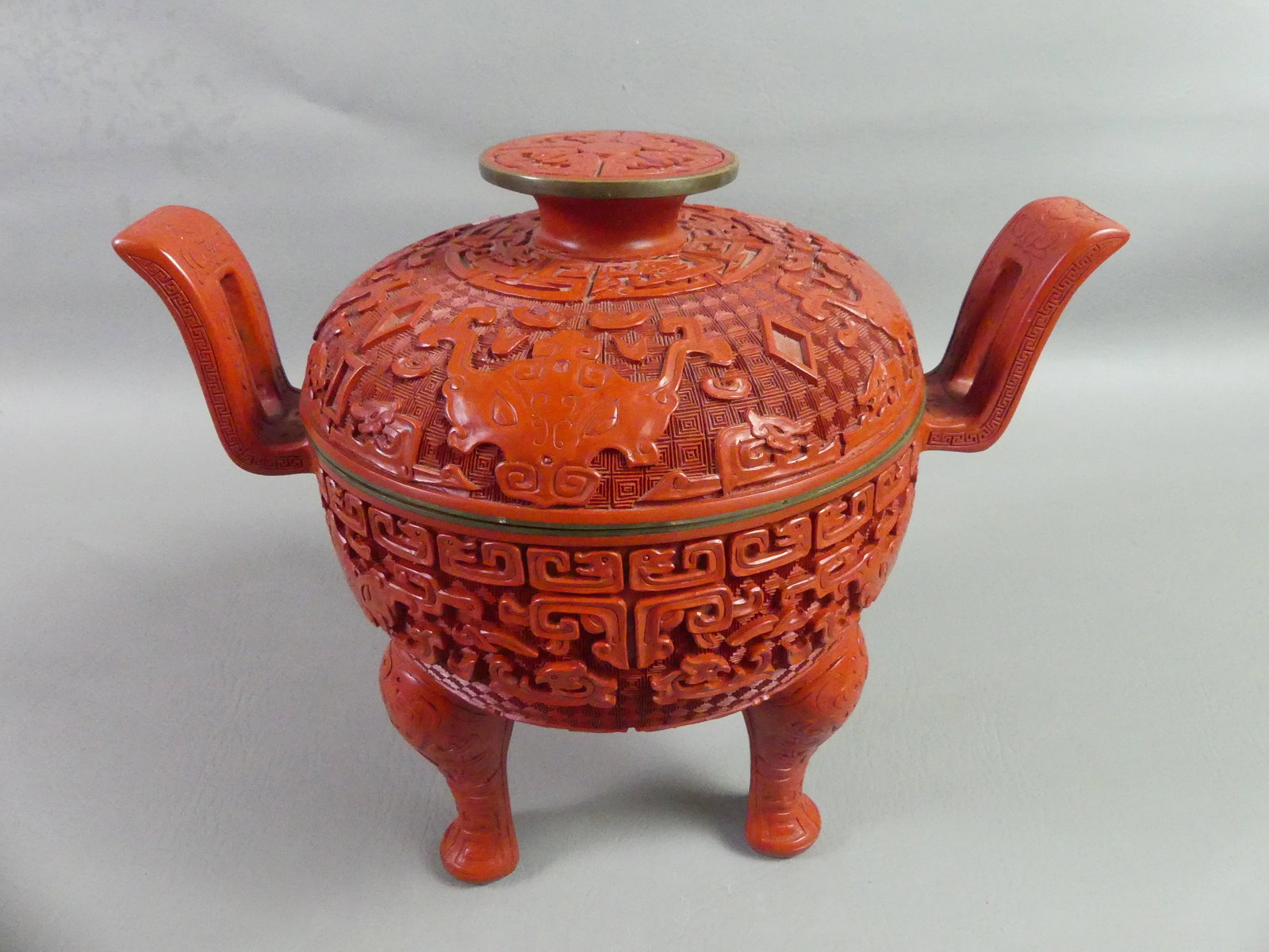 CHINESE CINNABAR TRIPOD CENSER: Large old carved cinnabar Chinese covered censer vase with handles. 10 in tall x 12 in wide. Black lacquer interior. VG condition.