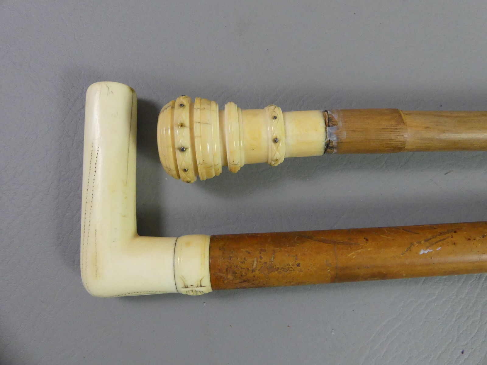 2 CARVED BONE CANES: Lot of 2 canes to 37 in long: Right angle carved bone handle with zipper and buckle design and cocabola shaft; and 3 in carved bone knob with inset 1870 US dime. Bamboo shaft.