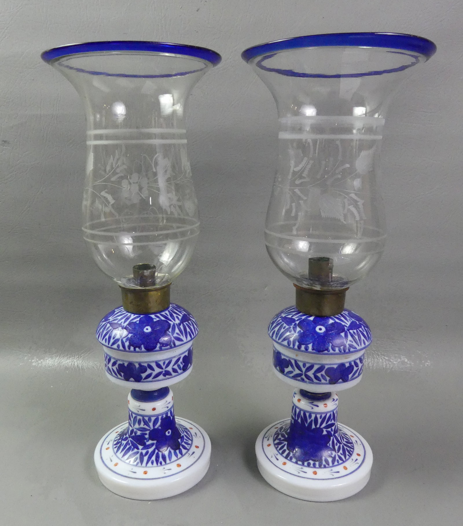 PAIR PAINTED GLASS OIL LAMPS: Pair of unusual painted milk glass antique oil lamps with etched and blown glass chimney shades (small crack bottom of one shade). Base is 8.5 in, overall 16.25 in tall.