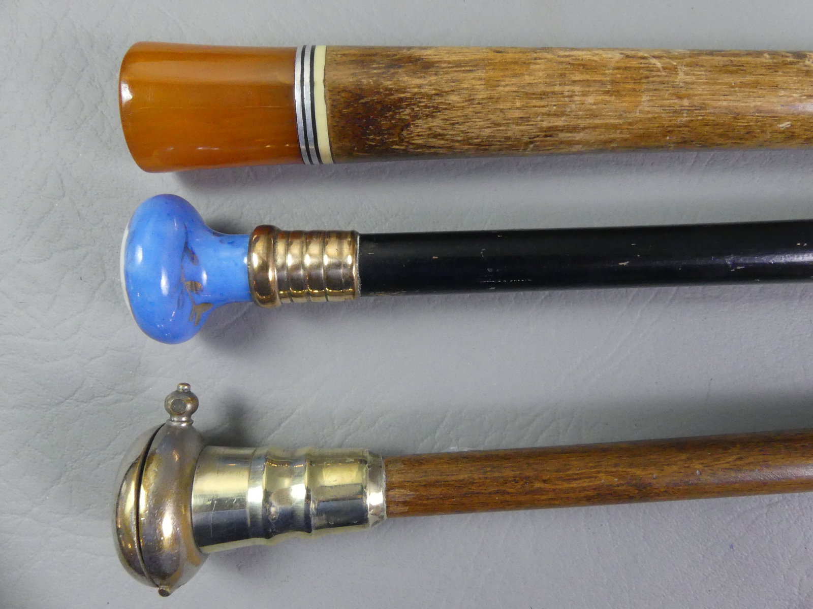 3 CANES INCL. NICKEL DISPENSER: Lot 3 canes to 37 in long: antique nickel dispenser with classical figure on hinged lid exposing spring-loaded compartment with nickels, 1.25 in diam; bakelite knob handled cane, 1.5 in; and porcelain