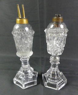 2 SANDWICH GLASS WHALE OIL LAMPS: Lot of 2 Sandwich flint glass whale oil lamps to 10.5 in tall with original brass double burners and hexagonal bases. Good condition, couple shallow flakes on underside of thumbprint lamp.