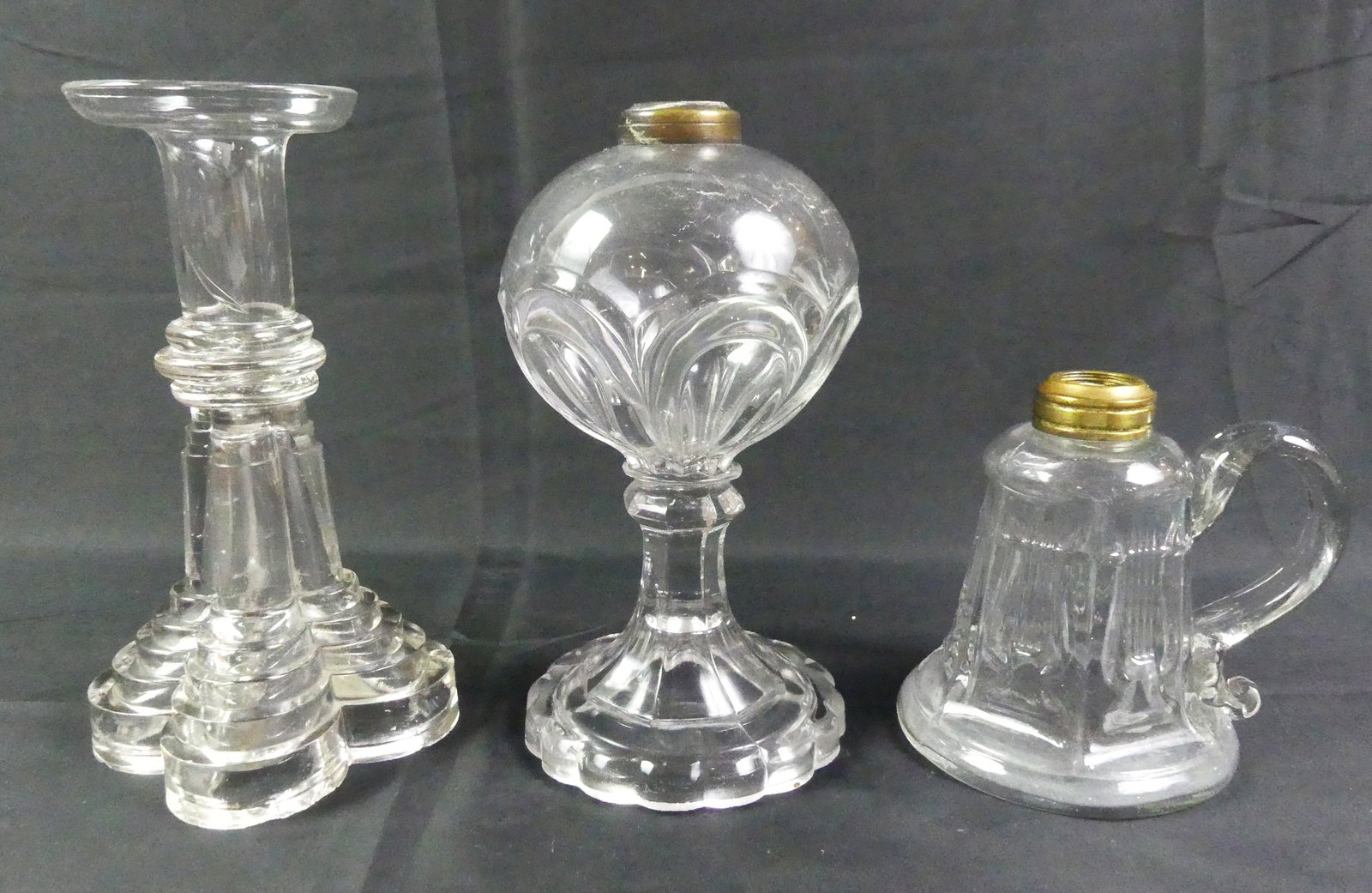 3 SANDWICH GLASS OIL LAMPS: Lot 3 Sandwich colorless glass oil lamps: Lyre pattern finger lamp, 5 in; 8 in candlestick with a waterfall base ; and 7.5 in lamp with bulbous font. All VG condition.