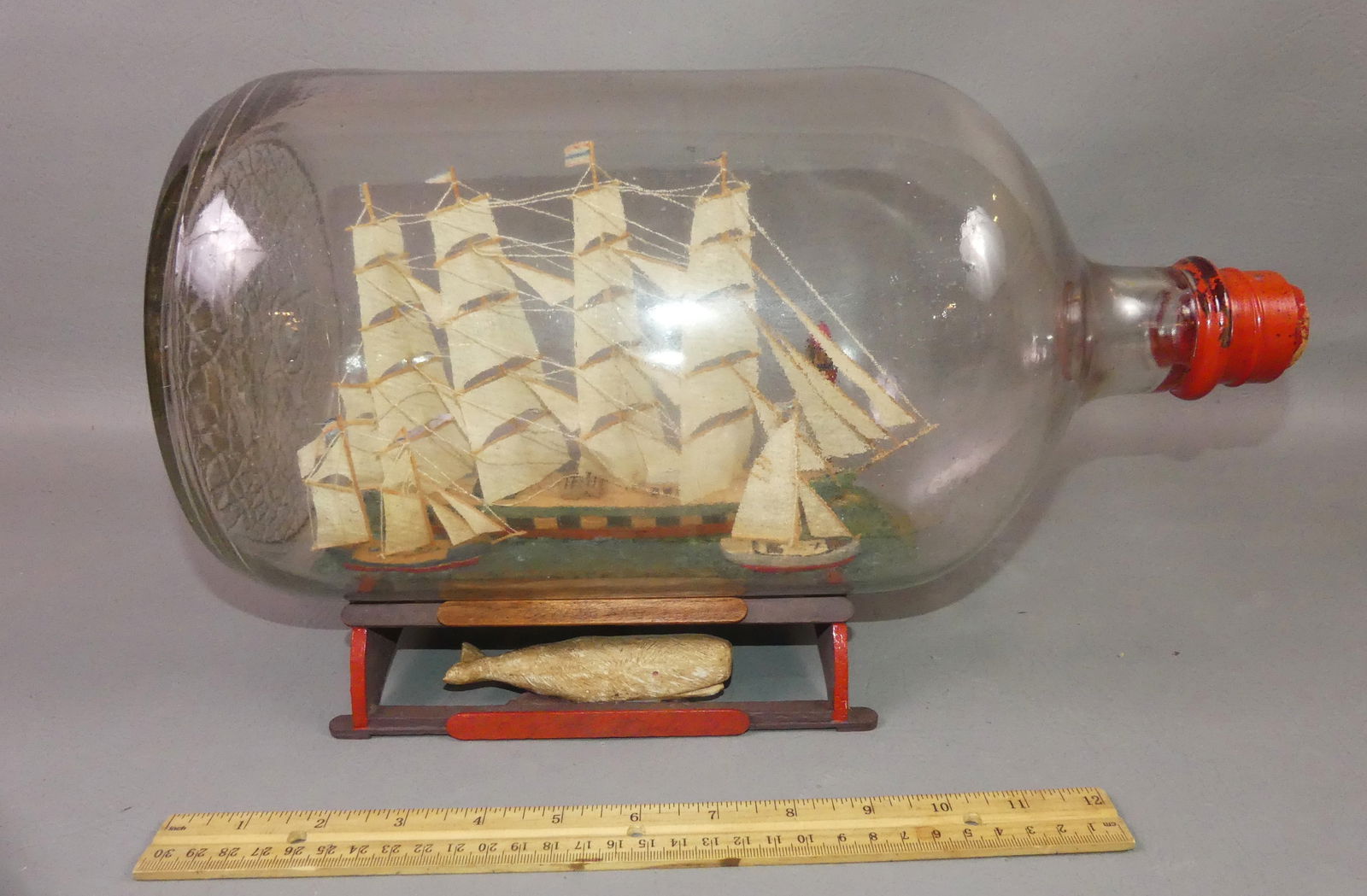 LARGE SHIP IN BOTTLE: Large ship's in glass bottle with wood base having carved whale. There are 3 different ships and a lighthouse inside. 16 in long x 8 in diameter.
