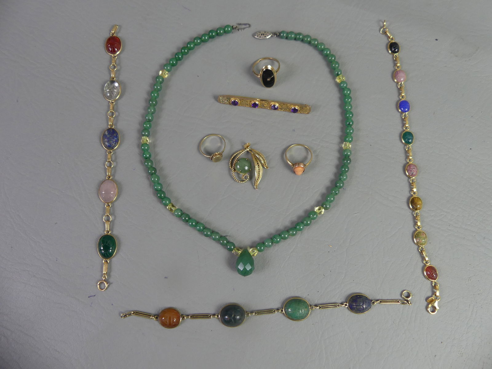 LOT MOSTLY GOLD JEWELRY & SCARAB BRACELETS: Lot of 9 pieces of jewelry: Jade bead necklace, 18 in long, with silver or white gold clasp; 3 scarab gemstone bracelets to 7.5 in long; amethyst and gold pin/brooch; gold pendant with jade stone; and