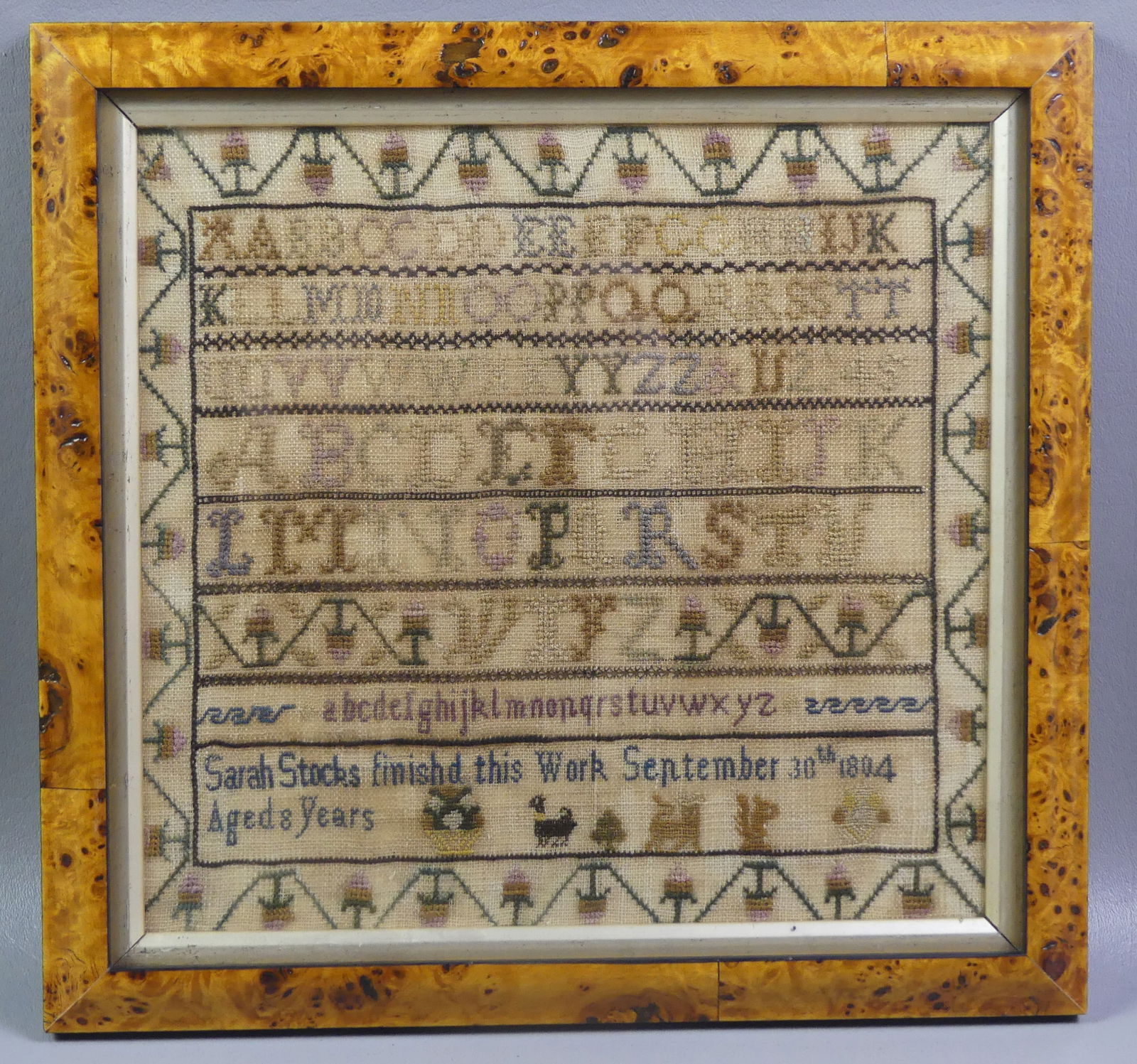 1804 SAMPLER BY SARAH STOCK: Framed Anglo-American sampler dated 1804 by Sarah Stock, dated Sept. 30, 1804, Aged 8 years. Includes alphabet, animals, and floral border. Overall 12 x 12 in framed. NOTE: We can ship this item