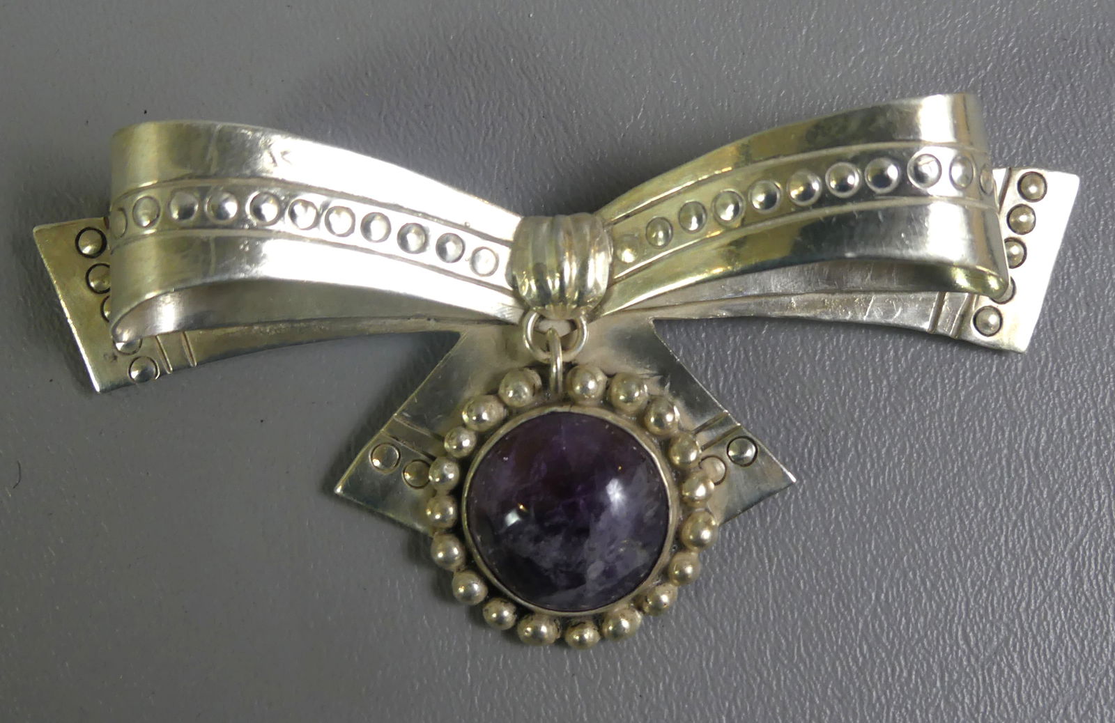 SPRATLING MEXICAN LARGE STERLING BROOCH: Large ribbon-form sterling silver brooch with center polished 19mm amethyst stone signed Spratling, Mexico. 4.5 in wide and 2 in high. Weighs 2.25 ozt. NOTE: We can ship this item in-house.