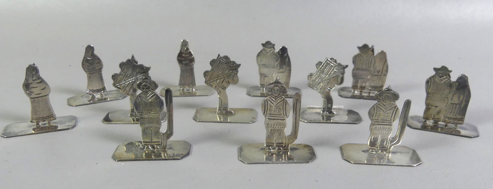 12 MEXICAN STERLING PLACE CARD HOLDERS: Set of 12 Mexican sterling silver place card holders signed Sanborns with 4 different embossed genre scenes. 1.5 in high, total 5.34 ozt. NOTE: We can ship this item in-house.