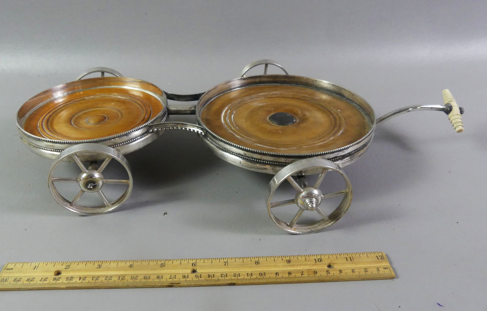 RARE SILVER PLATE WINE BOTTLE TROLLEY: Unusual antique double-wine bottle trolley with silver plated frame having a carved bone handle with moveable front wheels. Wooden base. No marks, circa 1900 probably English. 19 in long x 3 in high,