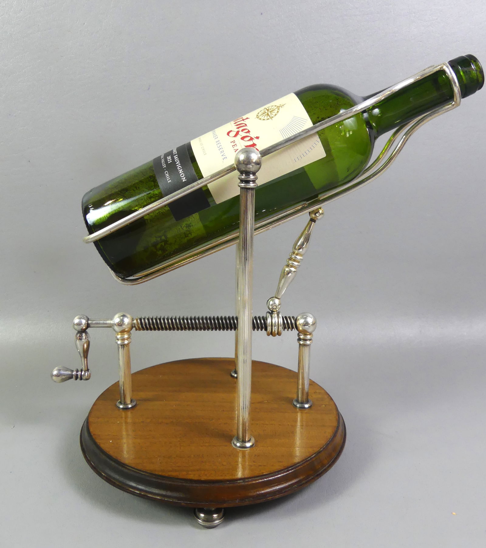 CHRISTOFLE SILVER WINE BOTTLE POURER: Scarce silver plated wine bottle cradle screw-crank to lower bottle and pour. Stamped Christofle, France with hallmarks. 12 in high, 8 in diameter, wood base. NOTE: We can ship this item in-house.