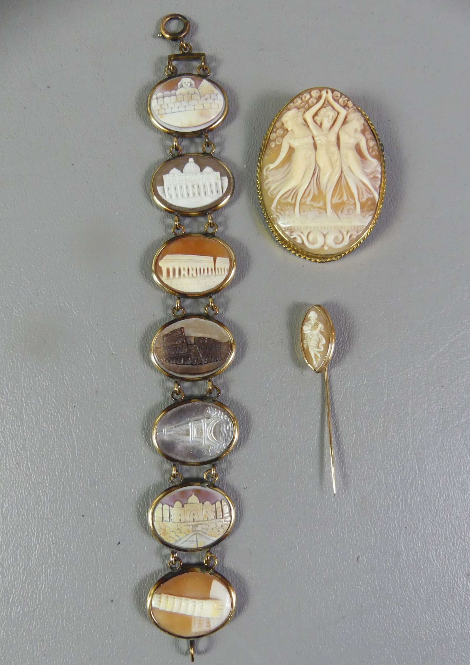 3 PIECES GOLD & CAMEO JEWELRY:: 3 pieces of jewelry: 10k bracelet with unusual shell cameo carved segments with famous buildings (one abalone), 7 in long x 1 in wide; 9k oval cameo of the Three Graces, 2 x 1.5 in; and 10k hatpin wit