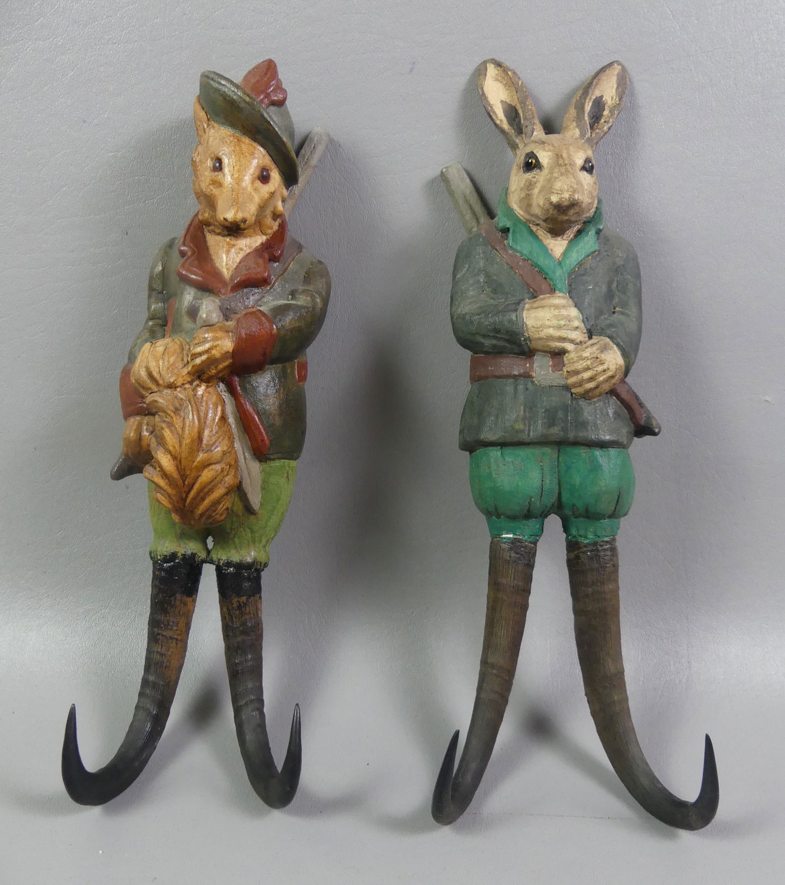 PAIR BLACK FOREST FIGURAL WALL HOOKS: Pair of Black Forest carved and polychromed wood wall coat hooks in the form of a rabbit hunter and fox hunter with curved antlers. Glass eyes. 13 in long. NOTE: We can ship this item in-house.