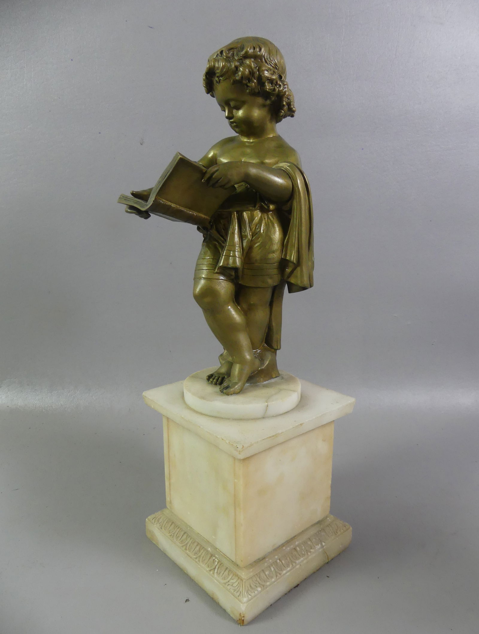 ANTIQUE FRENCH BRONZE - GIRL READING BOOK: Antique French bronze with golden patina depicting a young girl reading a book. Mounted on white alabaster base (glue repair at top). Unsigned, circa 1900. 18 in tall on the 6.5 in base. NOTE: We can