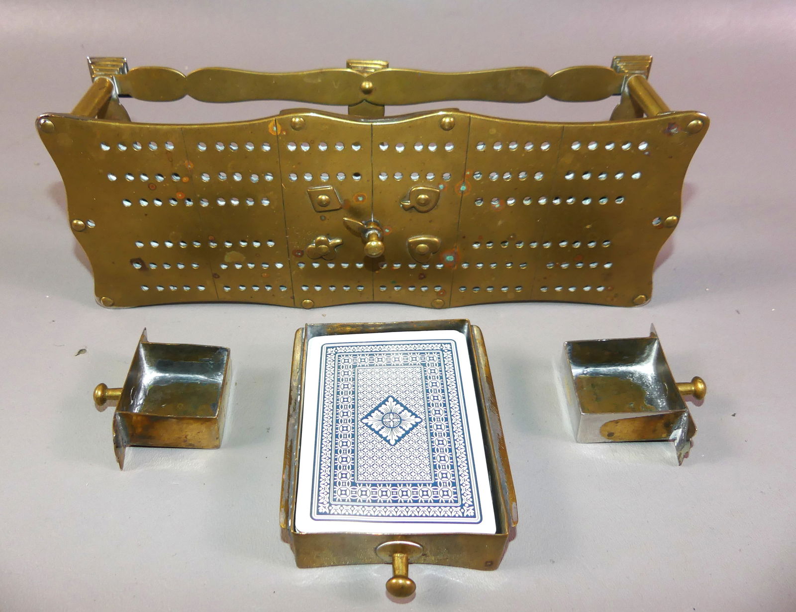 ANTIQUE BRASS CRIBBAGE BOARD: Unusual antique brass cribbage board with 3 drawers (one with modern playing cards). Center has pointer with card suits. 10 in long x 4 x 2.25 in high. NOTE: We can ship this item in-house.