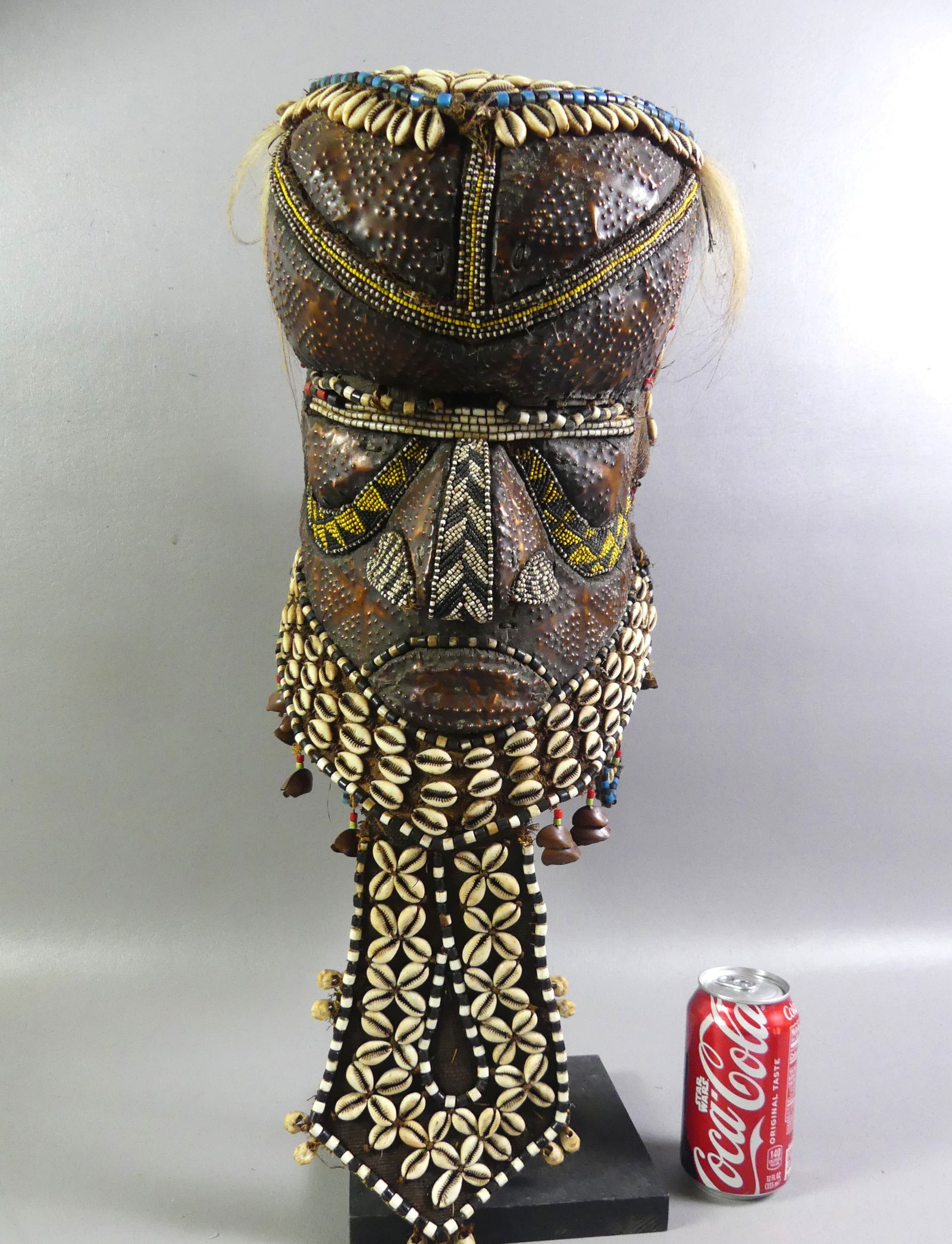 MIXED MATERIAL AFRICAN MASK: Vintage African humanoid mask made from mixed materials such as shells, copper, burlap, beads, etc. 24 in high.Comes with stand. NOTE: We can ship this item in-house.NOTE: We can ship this item