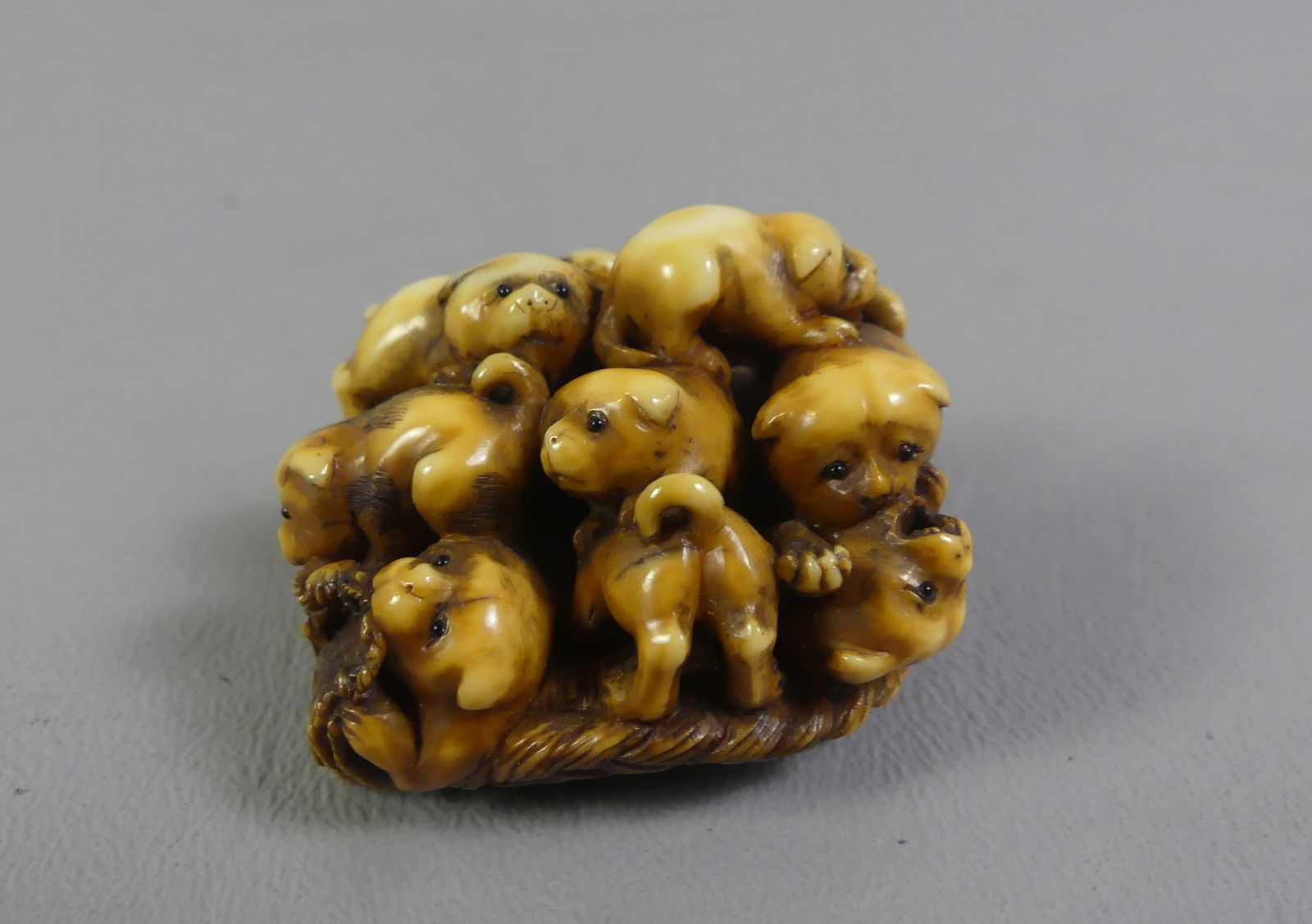 JAPANESE NETSUKE - BUNDLE OF PUPPIES: Antique Japanese carved netsuke of a bundle of puppies on a woven basket, one peering out from underneath. Signed. 1.5 x 1.25 x 1 inch. Ex-collection of Andrew C. Ware. NOTE: We can ship this item
