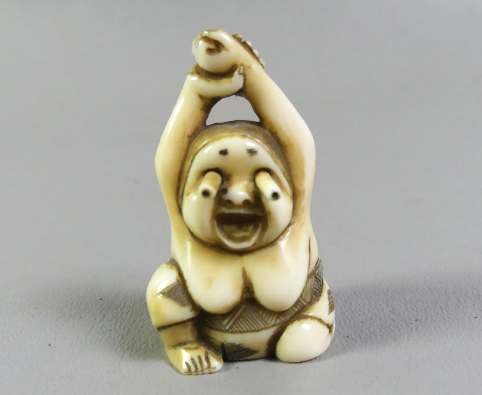 JAPANESE NETSUKE - WOMAN W/GOOGLY EYES: Antique Japanese netsuke depicting a semi-nude seated woman with arms above her head and 'pop out' eyes. Signed. 2 in by 1 in wide. Ex-collection of Andrew C. Ware. NOTE: We can ship this item