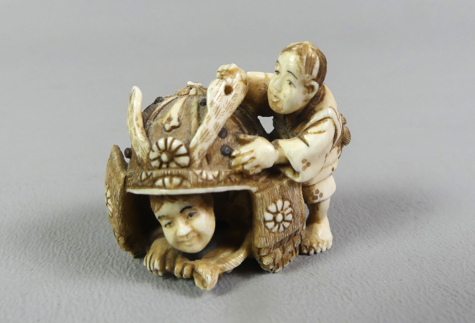 JAPANESE NETSUKE - SAMURAI HELMET: Unusual antique Japanese carved netsuke depicting 2 Asian men, one inside a huge Samurai helmet, signed. 1.25 x 1 inch. NOTE: We can ship this item in-house.