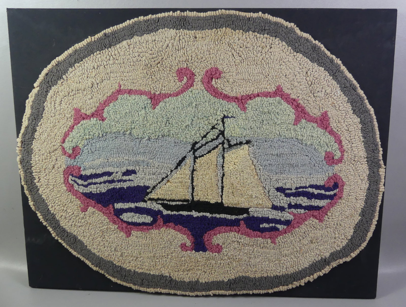 FRAMED HOOKED RUG OF SHIP: Old oval hooked rug of a ship, mounted on black fabric and stretcher for hanging. 28 x 36 in. Ca 1940. Note: We can ship this in-house.