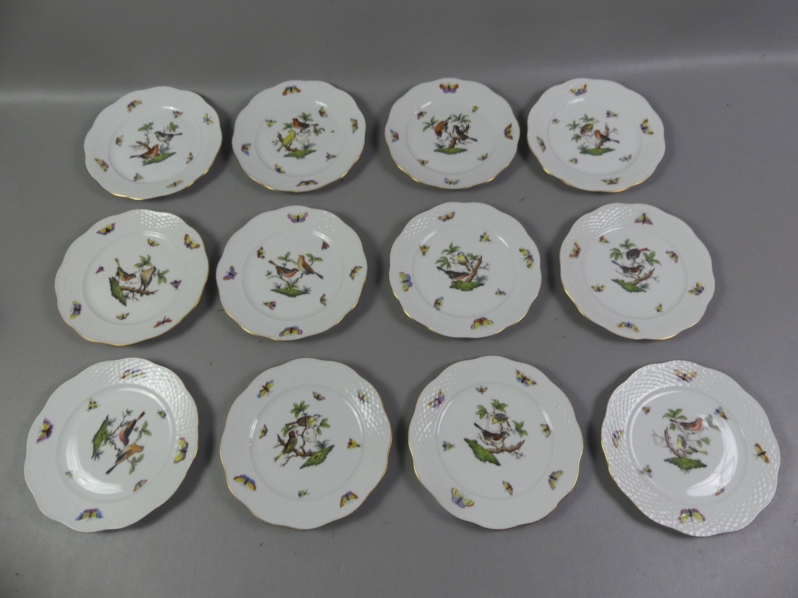 SET 12 HEREND PLATES - ROTHSCHILD BIRD: Set of 12 vintage Herend hand painted salad or dessert plates in the Rothschild Bird design having colorful birds and insects. They have a scalloped and gilt rim with basketweave design, #517. Size: