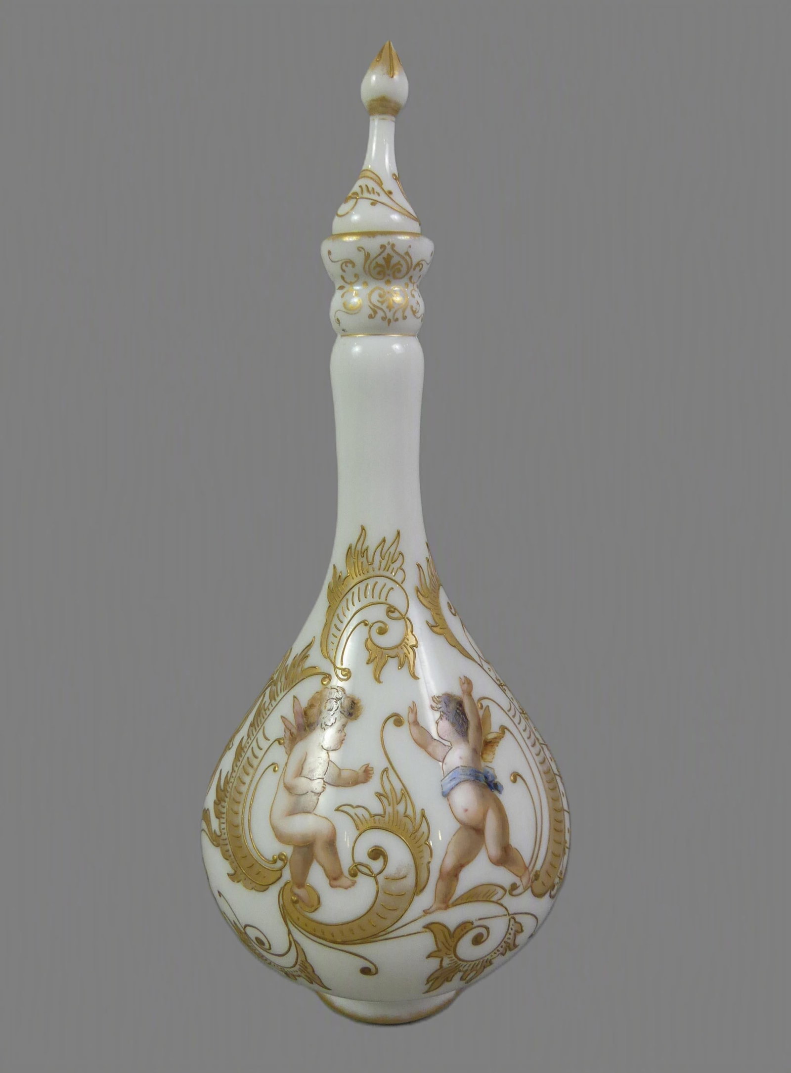 MT. WASHINGTON CROWN MILANO DECANTER: Rare Mt. Washington Crown Milano art glass bottle-form decanter with stopper. In opaque white glass with elaborate gilt designs and 3 winged cherubs. Has M wreath mark and number 1017 on base. 14.5