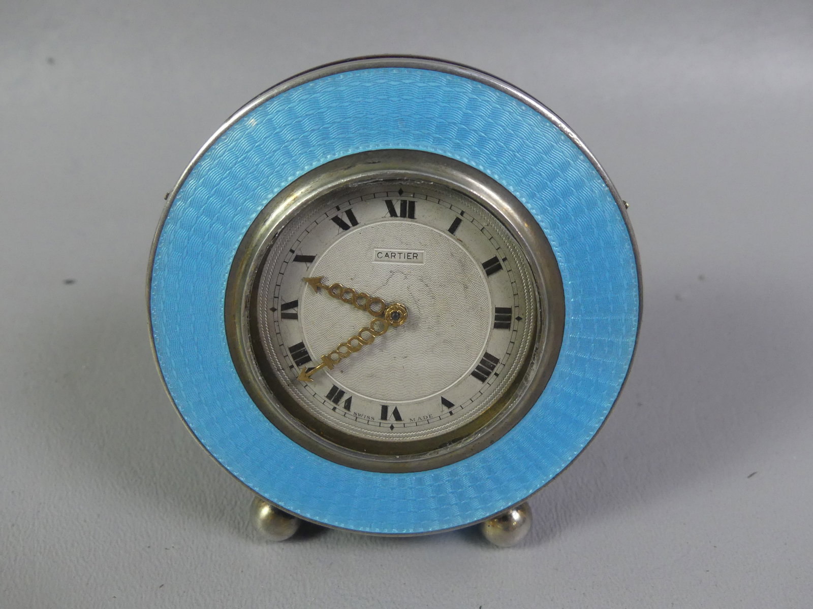 CARTIER SILVER & ENAMEL DESK CLOCK: Scarce Art Deco era Swiss made Cartier circular desk clock with guilloche blue enameled rim having rare palisander wood case. It is an 8 day key wind clock (key included). Back also signed Cartier NY