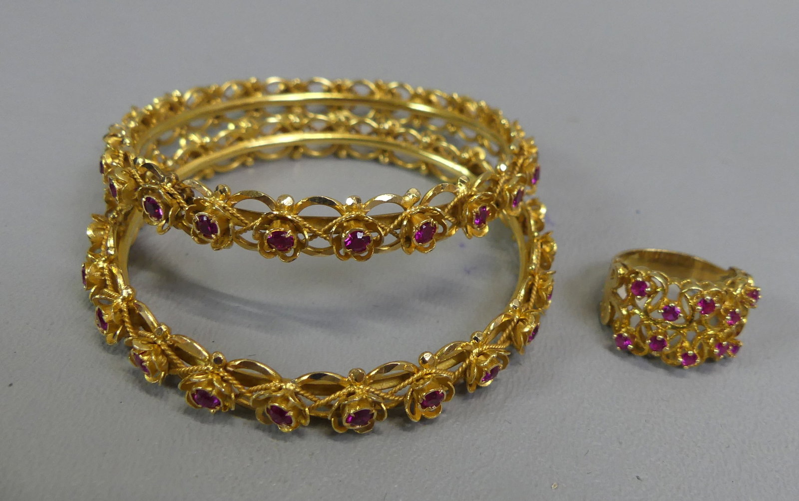 18K GOLD & RUBY BRACELETS & RING: Lot of 18k+ yellow gold jewelry: Pair of 1/4 inch wide bangle bracelets (hinged) inset with rubies; and size 6 ring set with rubies. Total 30.55 dwt.