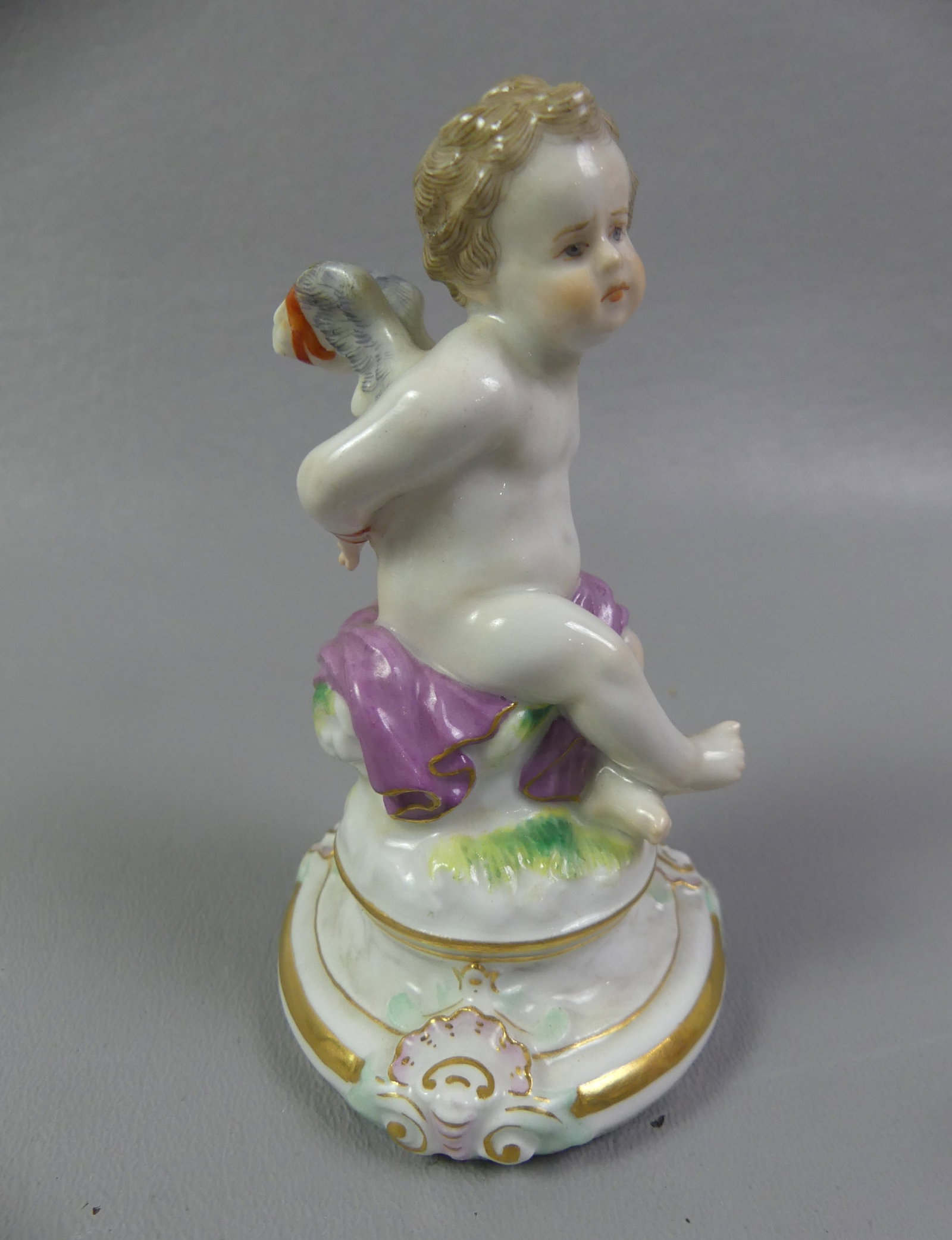 MEISSEN FIGURINE - BOUND GOD AMOR: 19th century Meissen porcelain figurine of a seated and bound god of love Amor. Modeled by Heinrich Schwabe. Has blue underglaze crossed swords mark. 4.25 in tall, excellent condition.