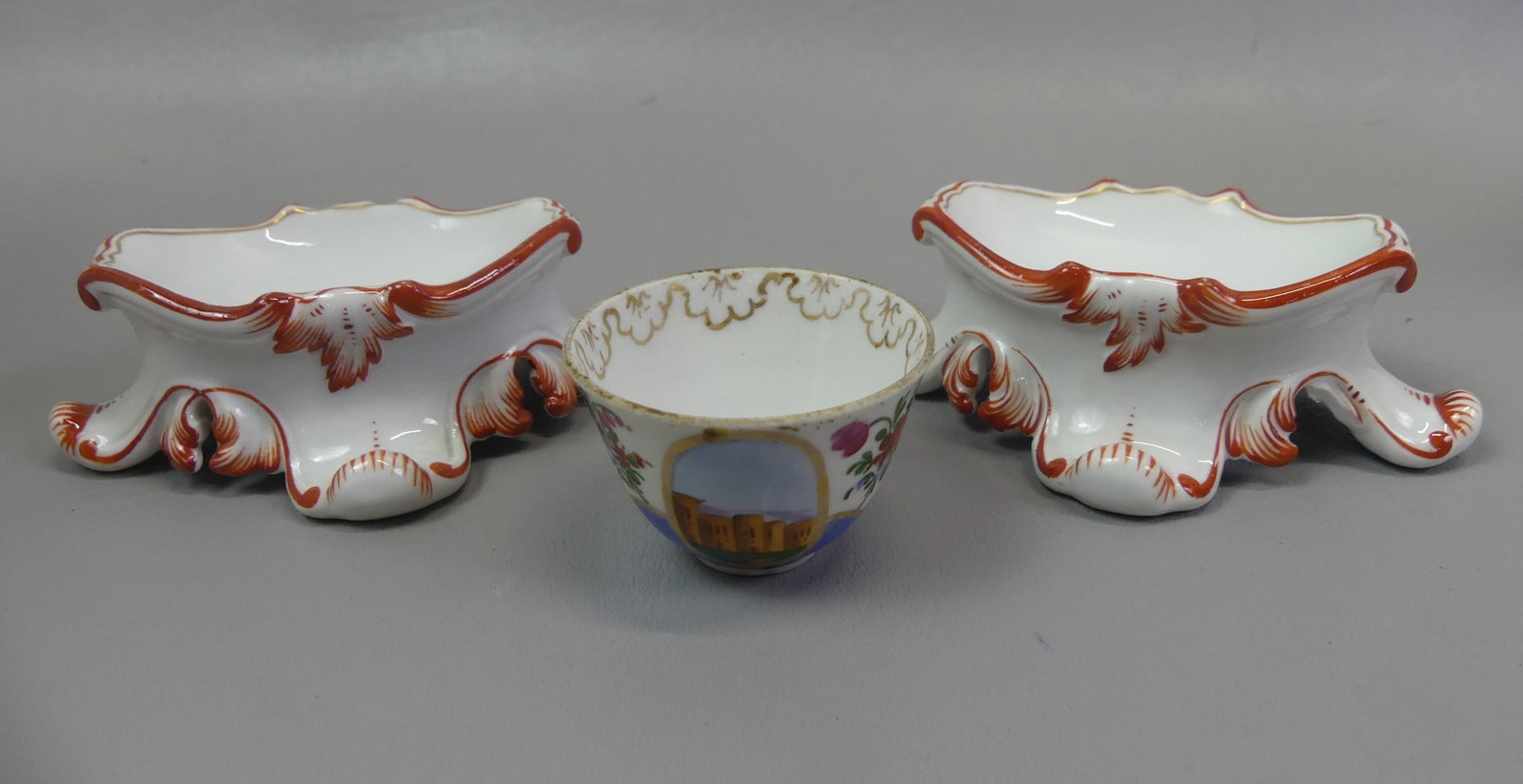 3 MEISSEN ITEMS: PAIR SALTS & CUP: Lot of 3 Meissen porcelain items: Pair of master salt cellars, 4 in long; and small shot cup with scenics and flowers, 2 in diam and 1.25 in high. All in VG condition.