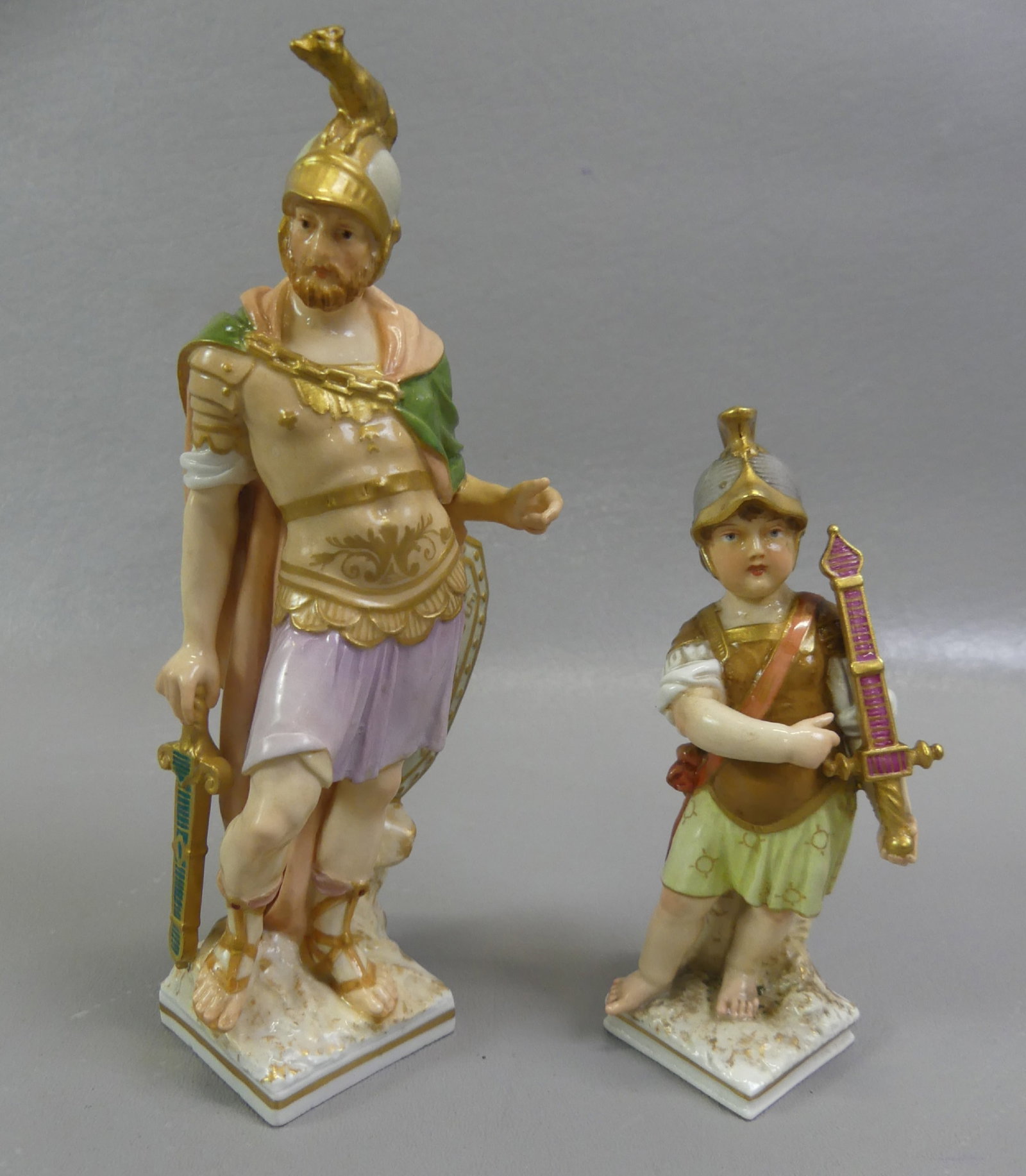 2 KPM FIGURES OF ROMAN SOLDIERS: Lot of two 19th century KPM (Royal Porcelain Factory of Berlin) figurines, both in Roman military attire: Man with shield and sword, 7 in tall; and child holding sword, 4.75 in. Both have blue