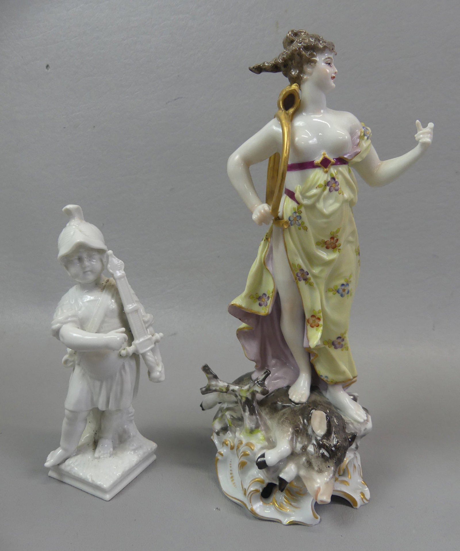 DRESDEN & KPM FIGURINES: Two antique porcelain figurines: Dresden 7.5 in tall figure of woman standing on a boar with hunting horn around shoulder (small chip on finger); and KPM blanc-de-chine figure of a Roman soldier, 5