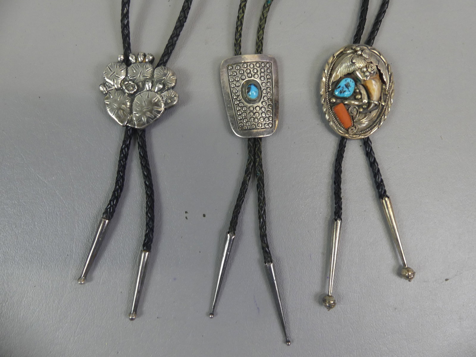3 NAVAJO SILVER BOLO TIES: Lot of 3 Navajo silver bolo ties: Natural claw with turquoise and coral signed RU, 2 in; Center turquoise stone signed Joe Anson; and Cactus signed Avery. Total on silver 4.25 ozt.
