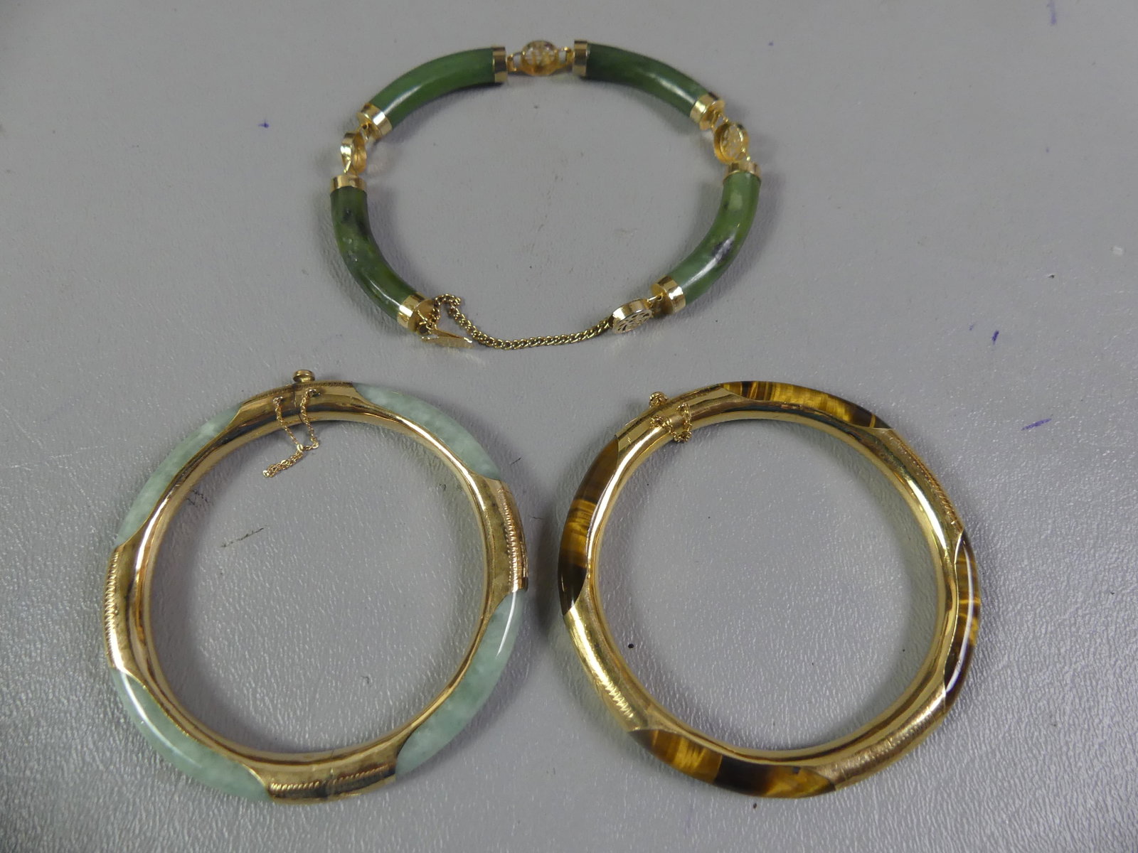 THREE 14K GOLD & GEM BRACELETS: Lot 3 bracelets with 14k gold mounts: 2 bangle style, one with jade and other with tiger eye, 2.25 in diameter; and green jade and gold Chinese bracelet with symbols. Total weight 42.75 dwt.