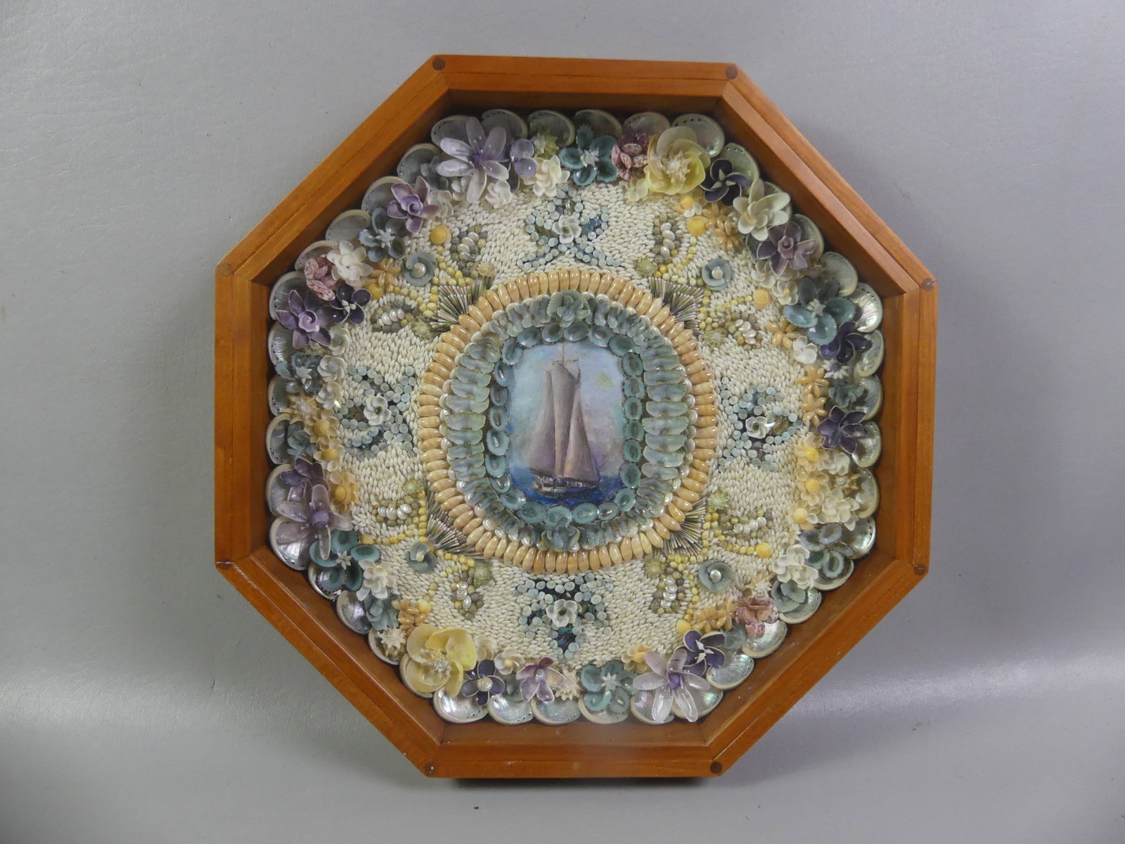 SEASHELL VALENTINE - PAINTED SAILBOAT: Vintage elaborate seashell valentine in hexagonal case with oval painted sailboat in center. 16 in diameter and 2 in deep.