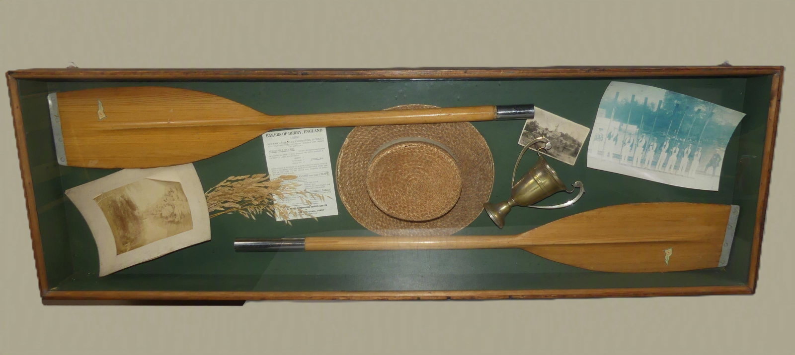 5 FT. SCULLING ITEMS IN SHADOWBOX: Large, old shadowbox with items from sculling including pair of oars (partial), photos, silverplated trophy cup, straw hat, etc. 61 in long x 19.5 x 5 in deep.