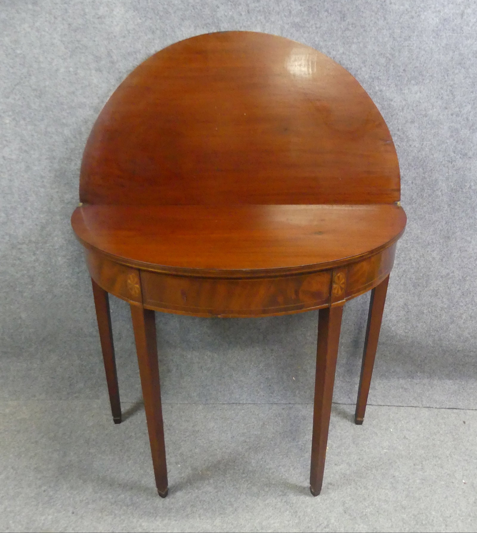 PERIOD HEPPLEWHITE CARD TABLE: Period American mahogany Hepplewhite card table with dem-lune shaped top and oval pinwheel inlay on skirt. 35 in wide x 28.5 h x 17 in deep (34 in when opened).