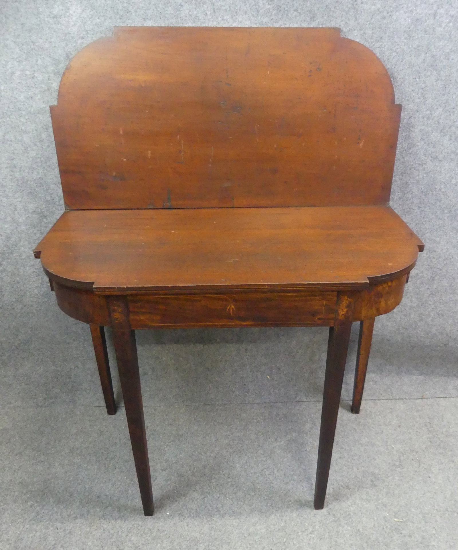 PERIOD HEPPLEWHITE CARD TABLE: Period American mahogany Hepplewhite card table with shaped top, and inlay. Has repair to leg, some surface imperfections. 35 w x 29 h x 17 in deep.