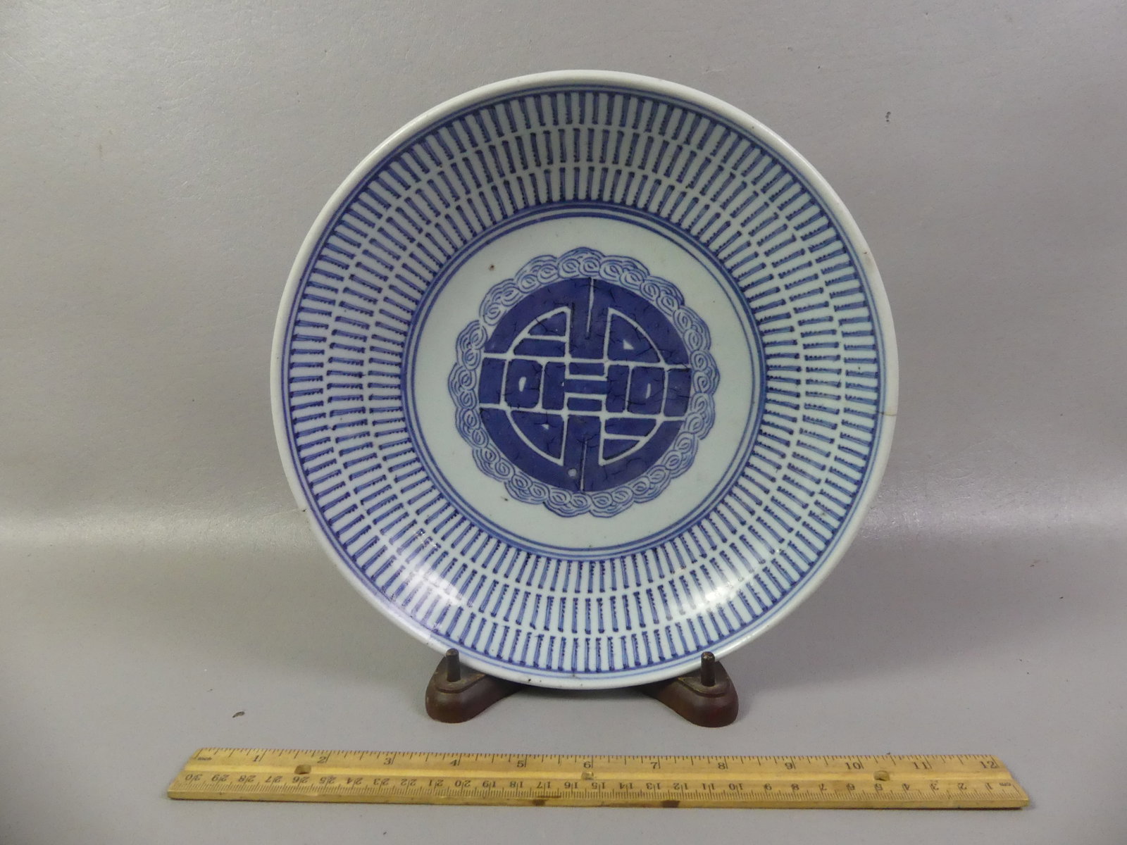 19TH C. CHINESE BLUE & WHITE SHALLOW BOWL: 19th century Chinese blue and white ceramic shallow bowl with picket design and symbol in center. Mounted on wood stand. 10 in diam by 2 in deep. Minor 1.5 in hairline.