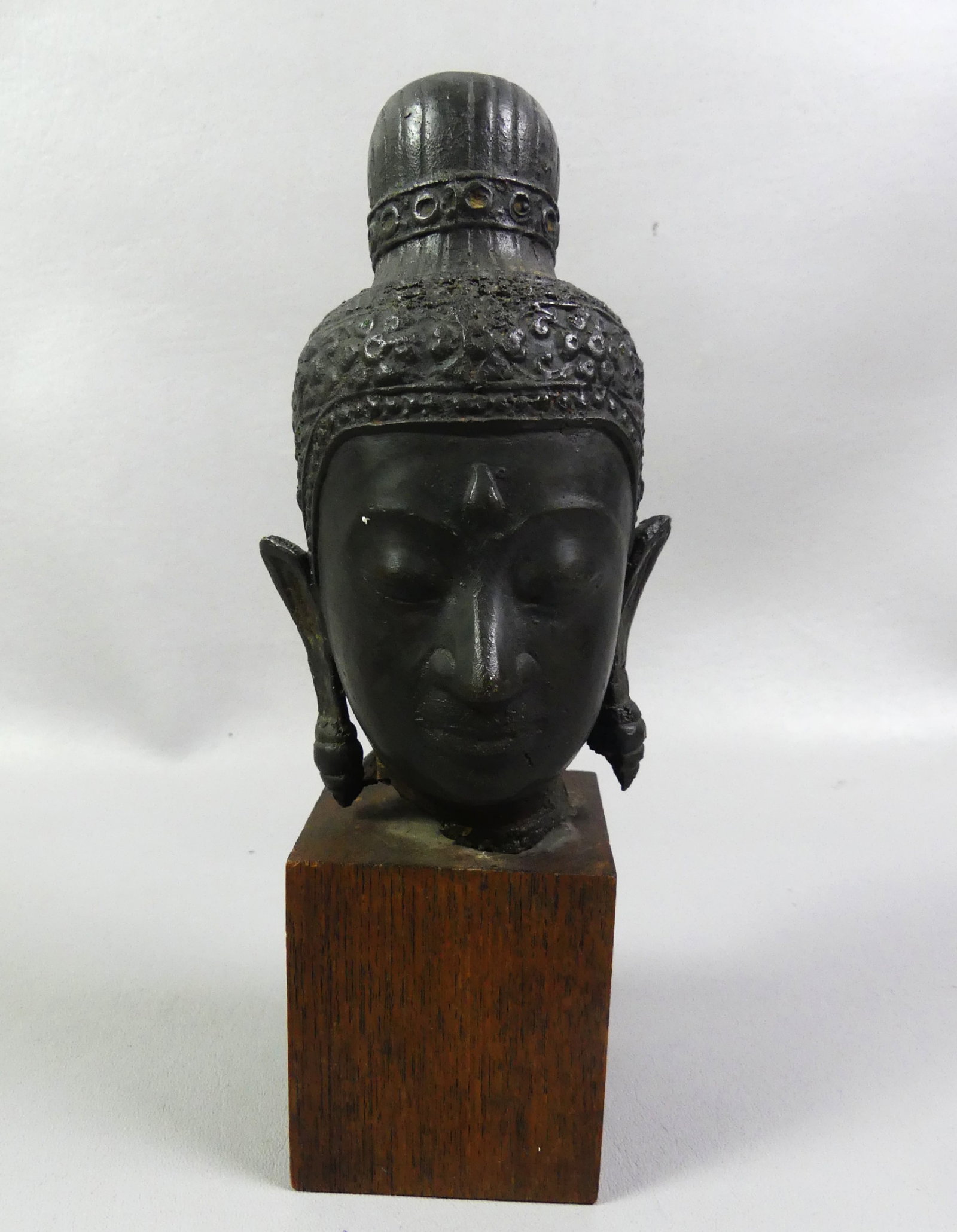 THAI BRONZE BUDDHA HEAD: Antique bronze buddha head with dark patina on 3 in high wood base attributed Thailand. 9 in tall overall.