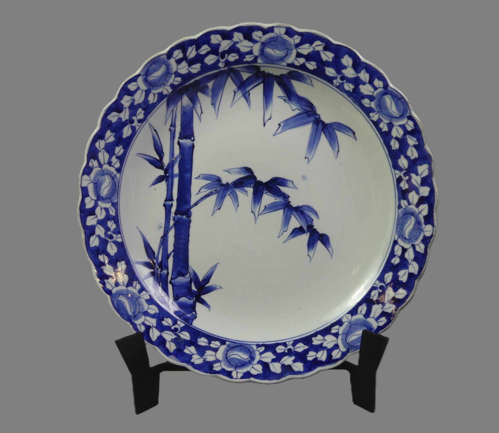 JAPANESE ARITA PORCELAIN CHARGER: Large 19th century Japanese Arita porcelain blue and white charger with bamboo trees design, mounted on metal stand. 17 in diameter with scalloped rim. VG condition.