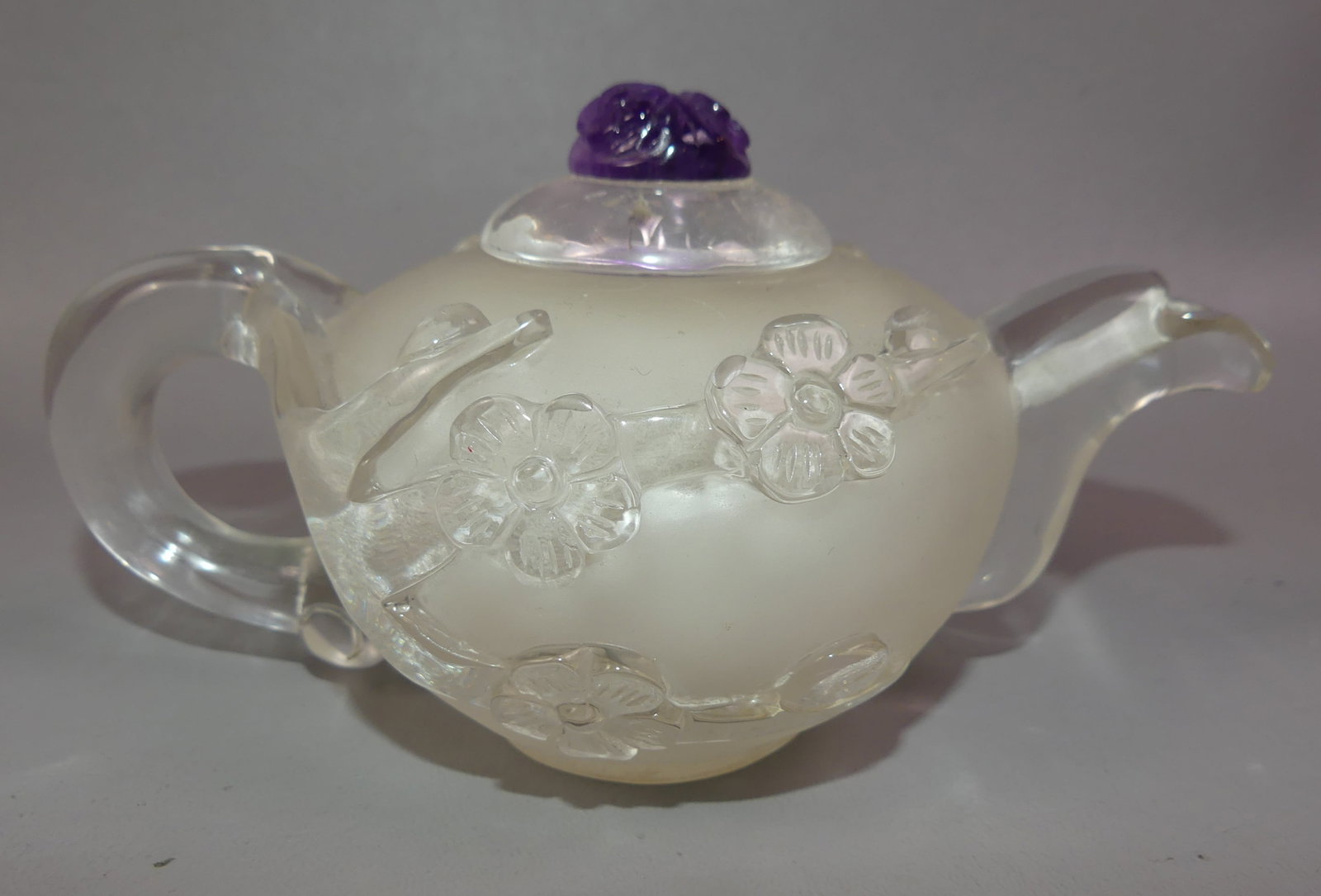 ROCK CRYSTAL MINI TEAPOT: Small carved rock crystal teapot with lid having amethyst floral finial. Weighs 20.9 oz or 594 grams. 6.5 in diameter and 3 in high.