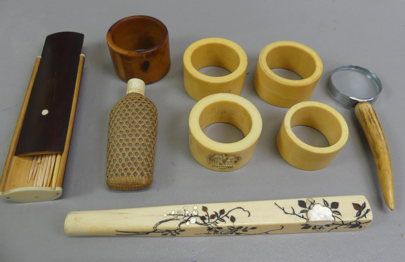 9 JAPANESE ORGANIC ITEMS: Lot of 9 mostly carved organic Japanese items including: 5 napkin rings, magnifier, 6.5 in inlaid parasol handle, 3 in glass flask with bone cap and woven exterior, and a wood toothpick holder.