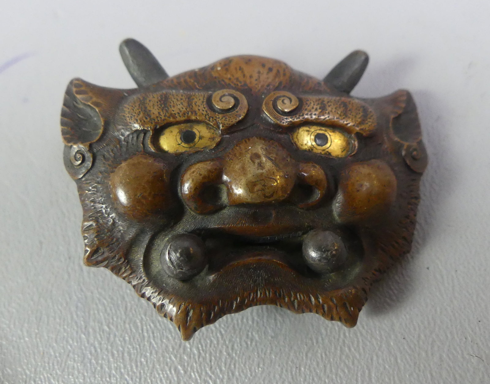 ANTIQUE JAPANESE BRONZE MENUKI - DEMON: Fine antique bronze Japanese menuki (ornamental sword element) in the form of a fierce Oni demon with inlaid gold eyes. 2.5 x 2 in. VG condition, attributed Edo or Meiji period.
