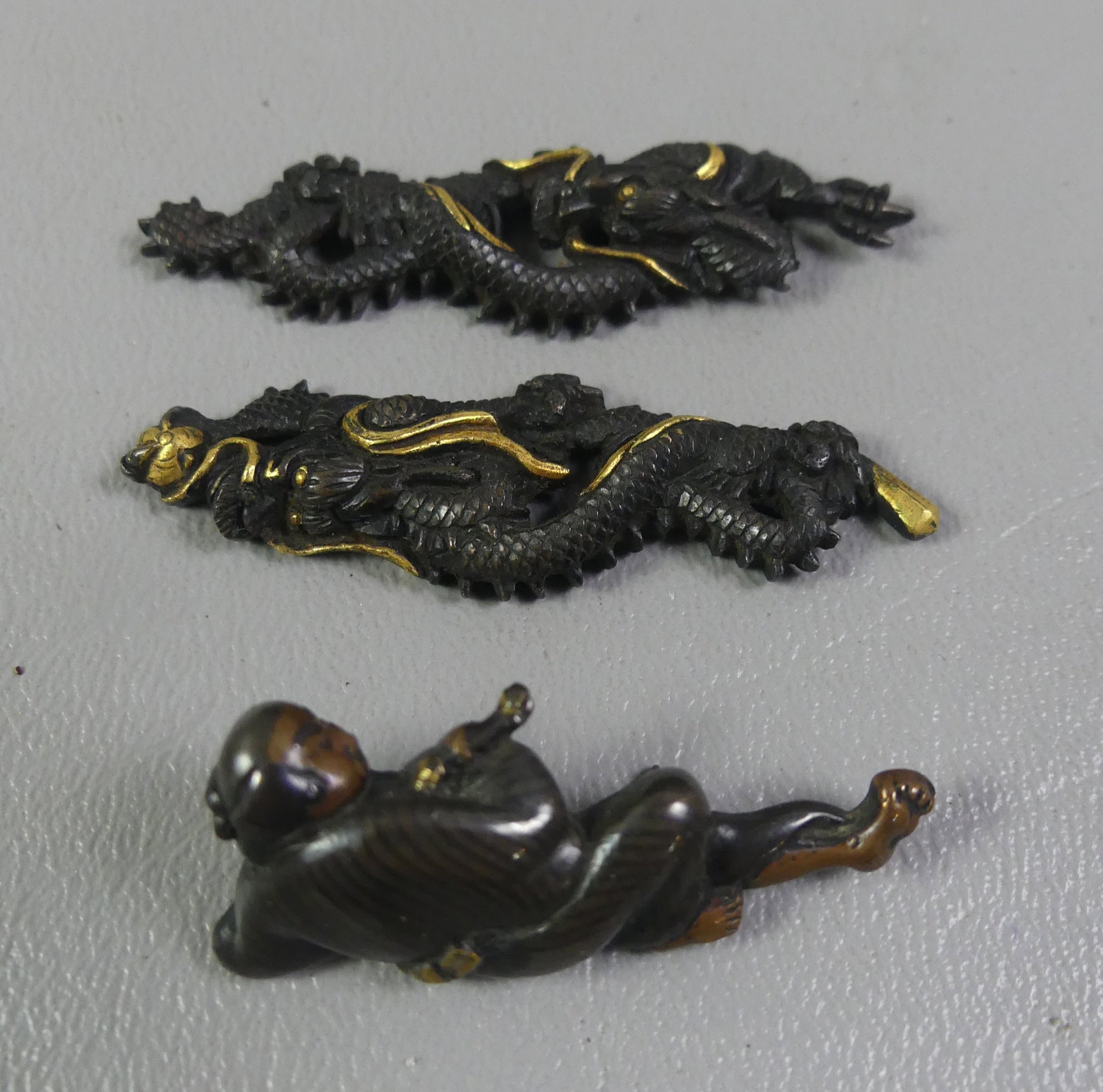 3 BRONZE MENUKI - GOTO SCHOOL: Lot of 3 antique Japanese bronze menuki (sword elements) including 1.5 in reclining man with gold overlay; pair of dragons, Goto School circa 1750, 2 in long, bronze with gold.