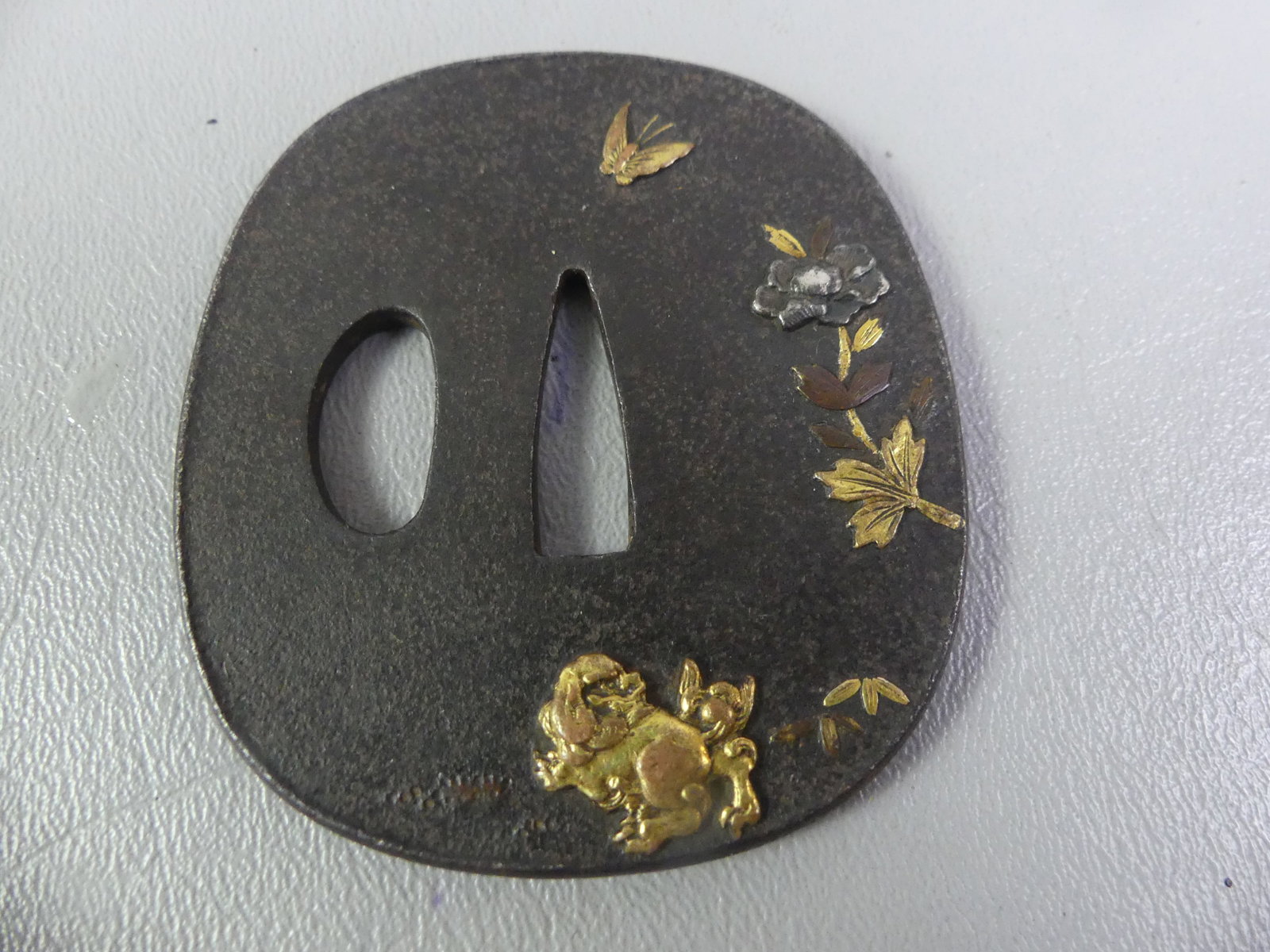 ANTIQUE IRON INLAID TSUBA - CREATURE: Edo period Japanese iron tsuba with mixed metal inlay (shakudo) of a creature, butterfly and flowers. Unsigned. 2.5 x 2.25 inches.