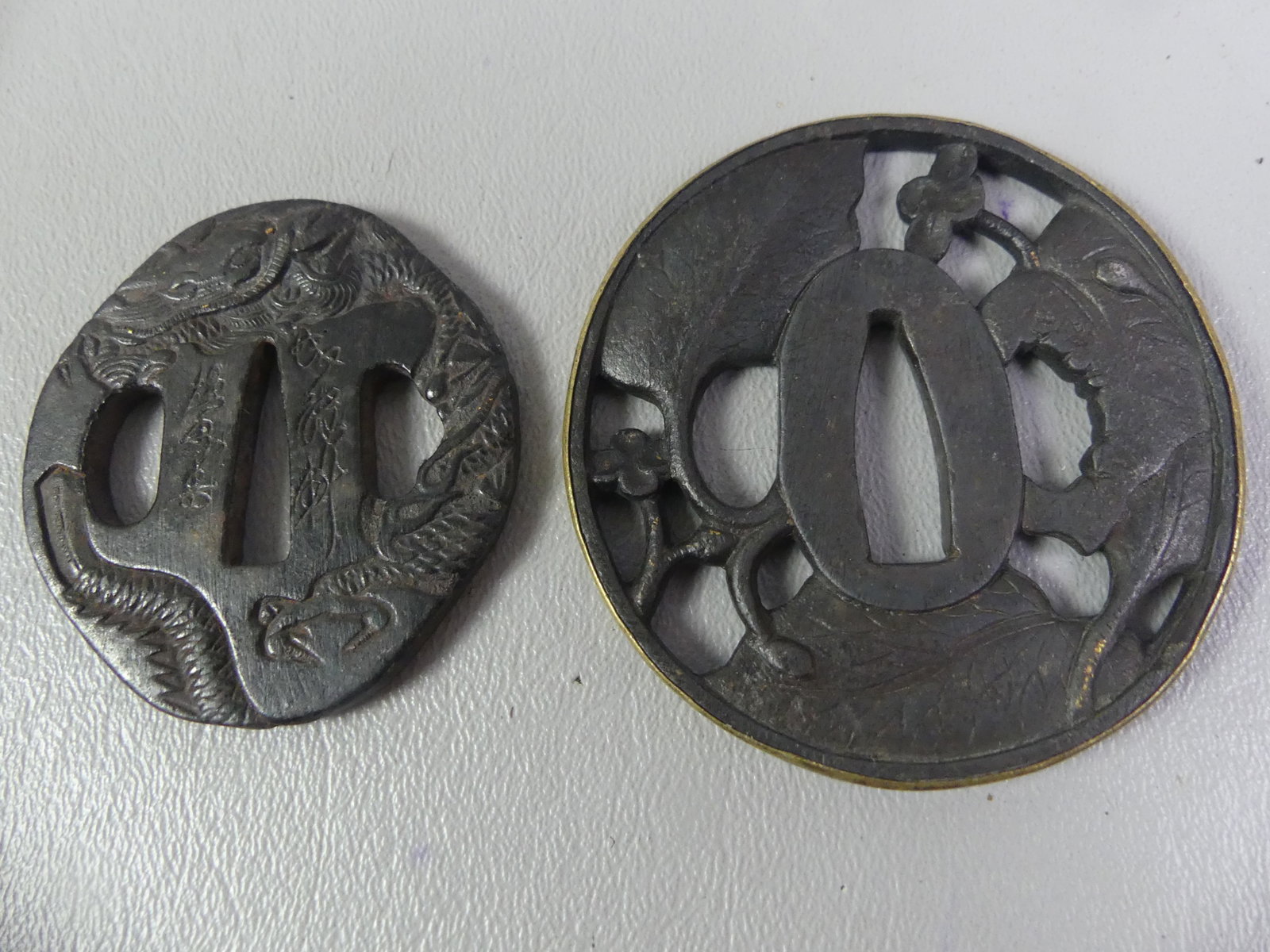 2 ANTIQUE IRON JAPANESE TSUBAS: Lot of 2 Edo period Japanese iron tsubas: 2 x 2 inch with embossed dragon; and 2.5 in with openwork floral design with brass bezel. Both unsigned.