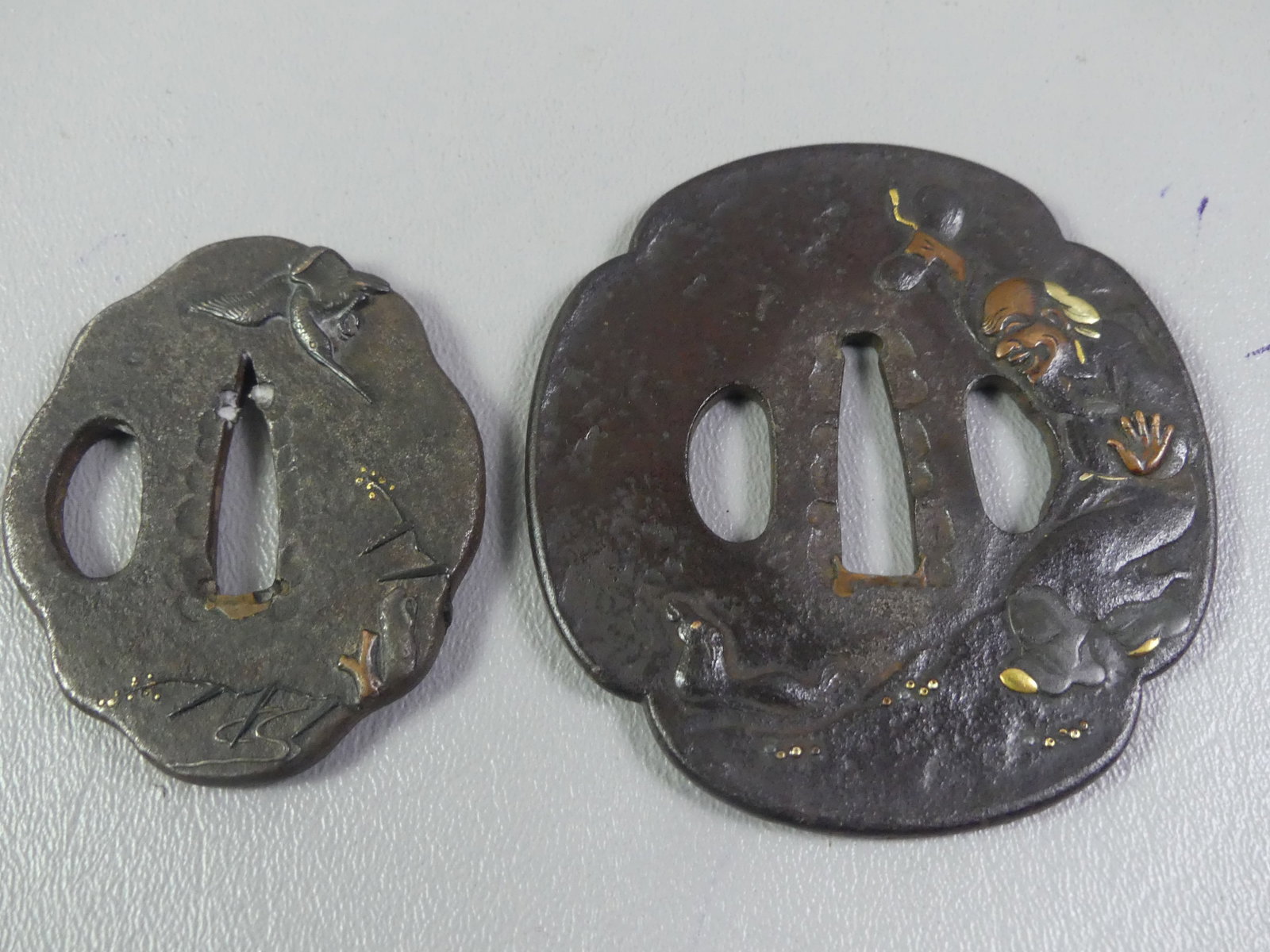 2 ANTIQUE TSUBAS - MAN & CRANE: Lot of 2 Edo period Japanese iron tsubas: 3 x 2.75 in of a man feeding a duck with mixed metal inlay. Has landscape on reverse. Unsigned. Together with a 2.25 x 2 inch iron tsuba with mixed metal