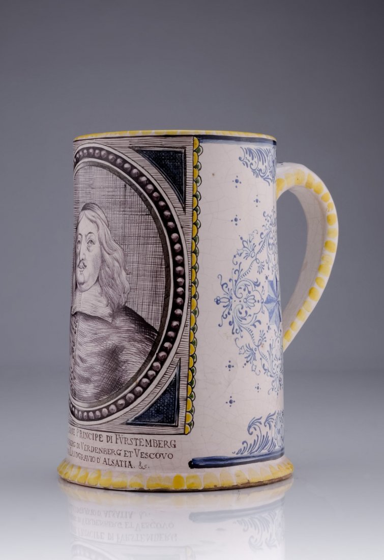 Grosser Walzenkrug "Franz Egon von: Grosser Walzenkrug "Franz Egon von Fuerstenberg-Heiligenberg". Wohl 19th cent. Faience, roetlicher Scherben. Graeulich-weiss glasiert und mit polychromen Muffelfarben staffiert. Schauseitig ein Bildni